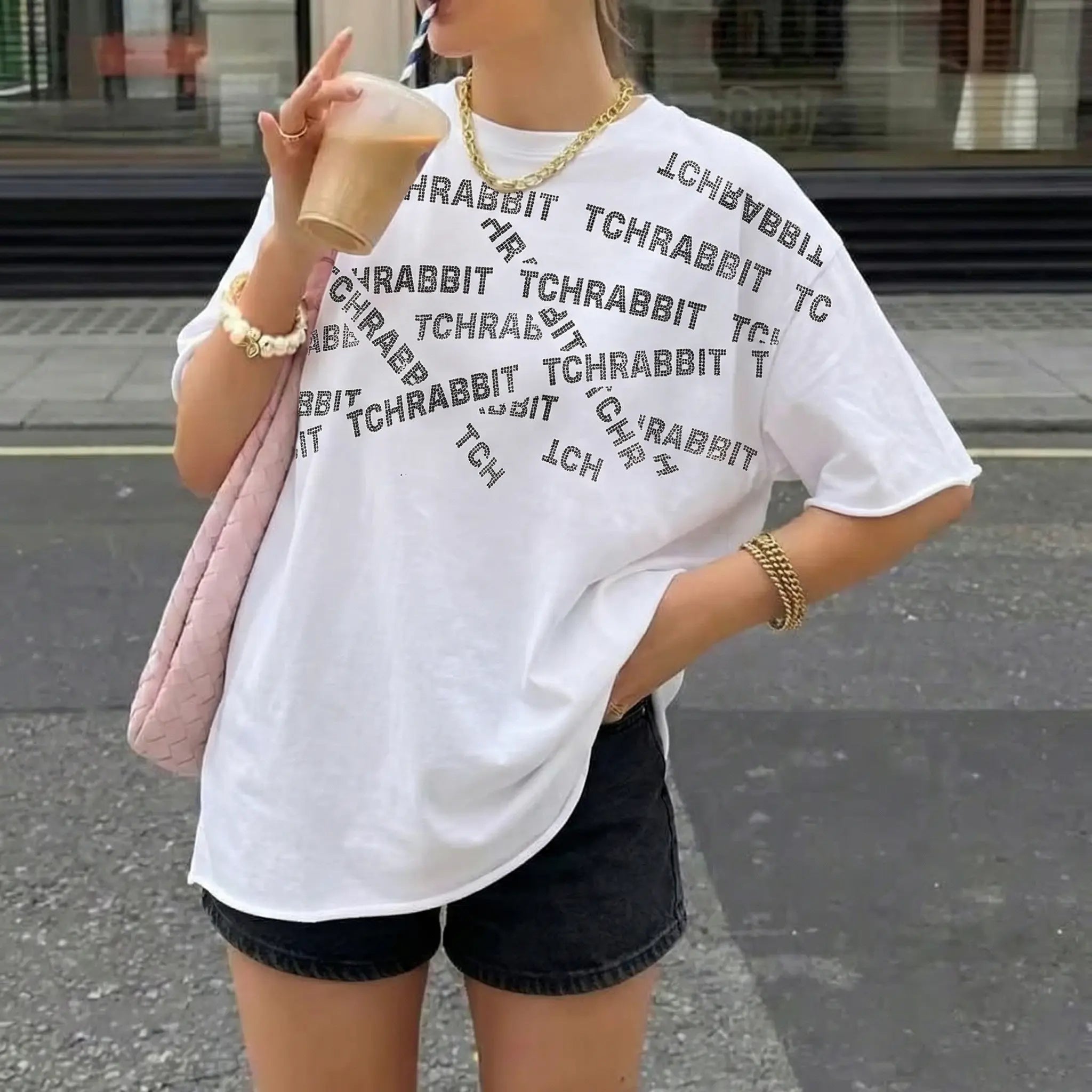 Person wearing a white t-shirt with text, holding a pink bag on a street. TCH All-Over TCHRABBIT Logo T-Shirt