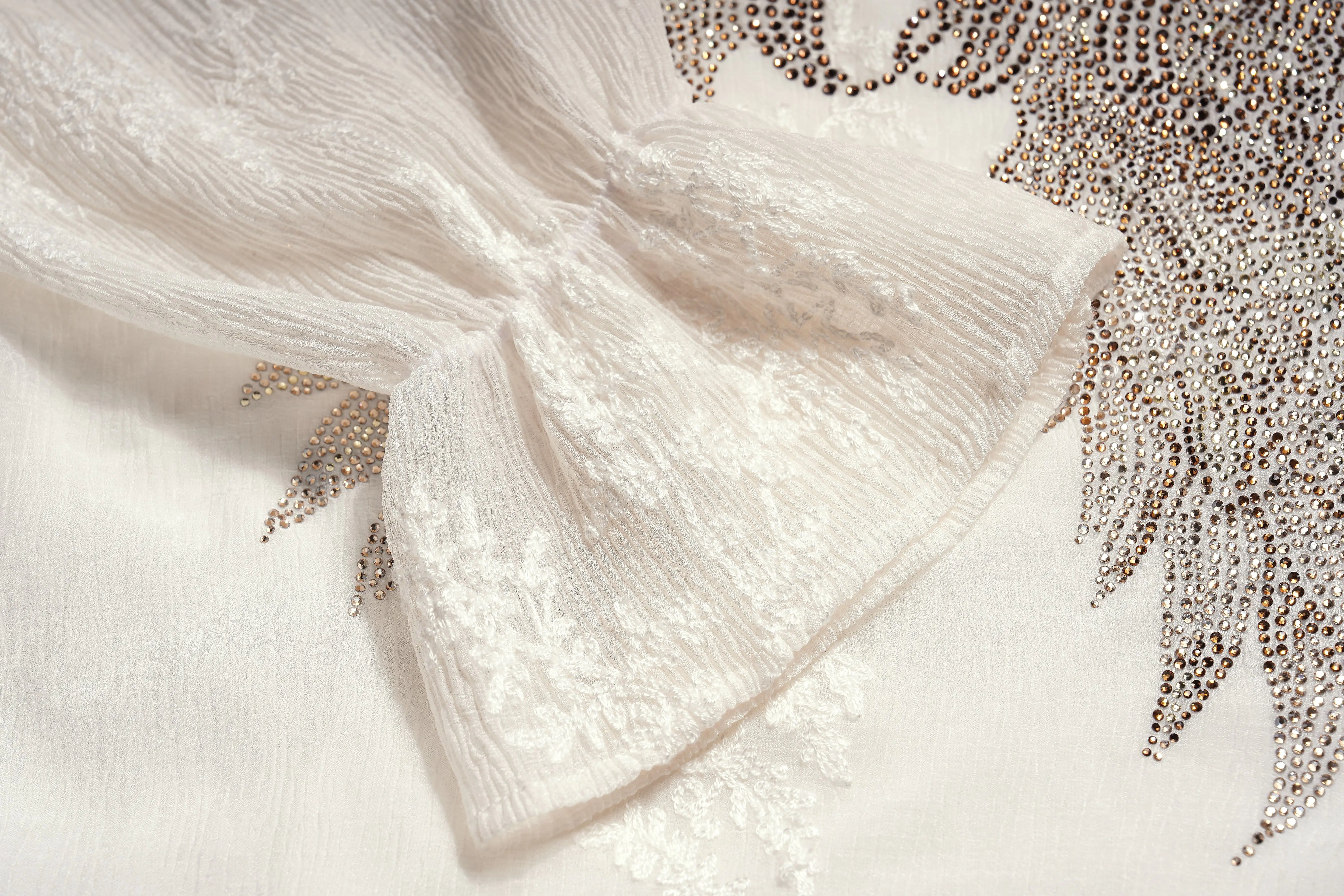 Close-up of a white fabric with gold embellishments on a light background, TCH Angel Wings Rhinestone Ruffle Blouse