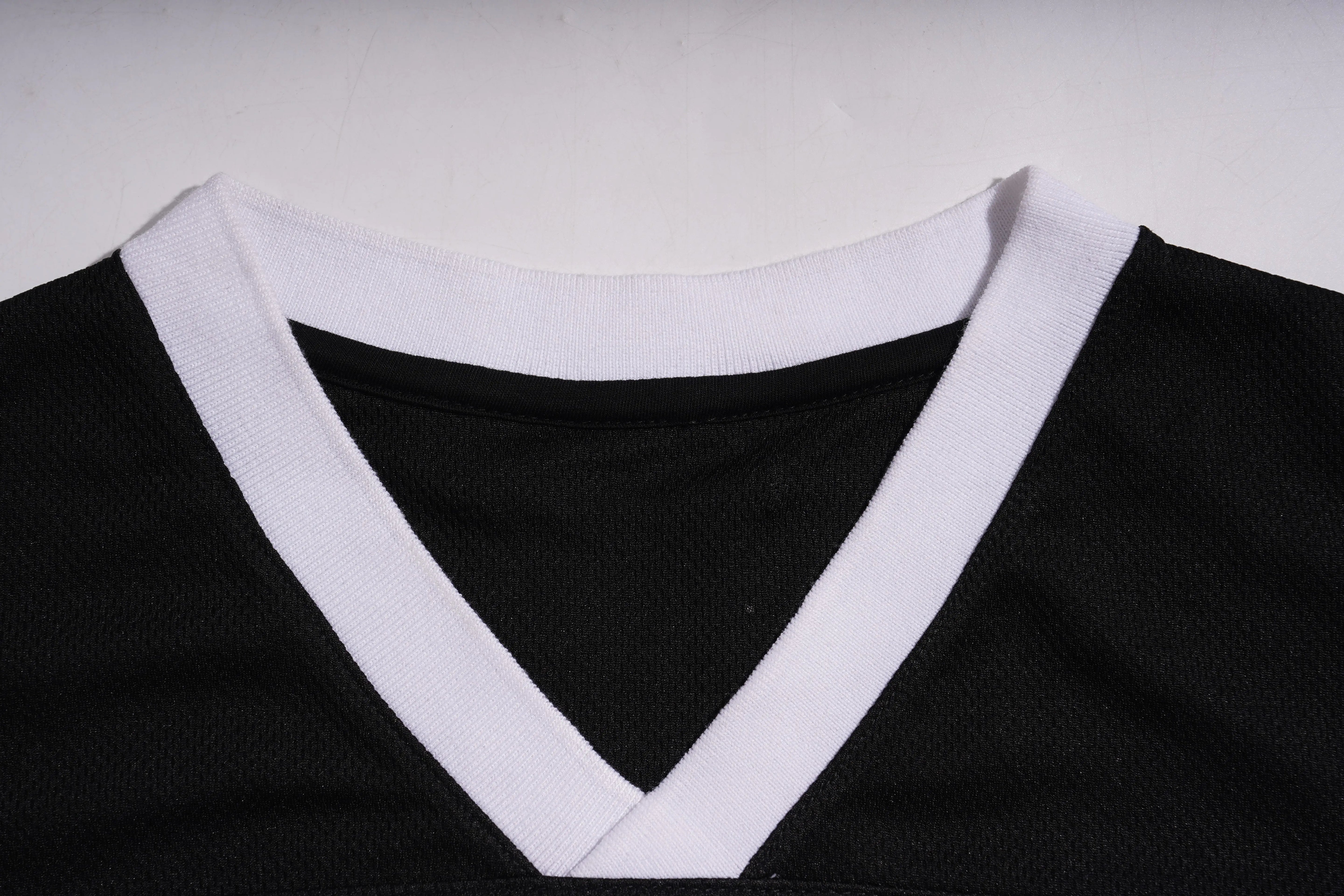 Close-up of a black jersey with white trim on a plain background, TCH Angel Wings Rhinestone V-Neck Tee