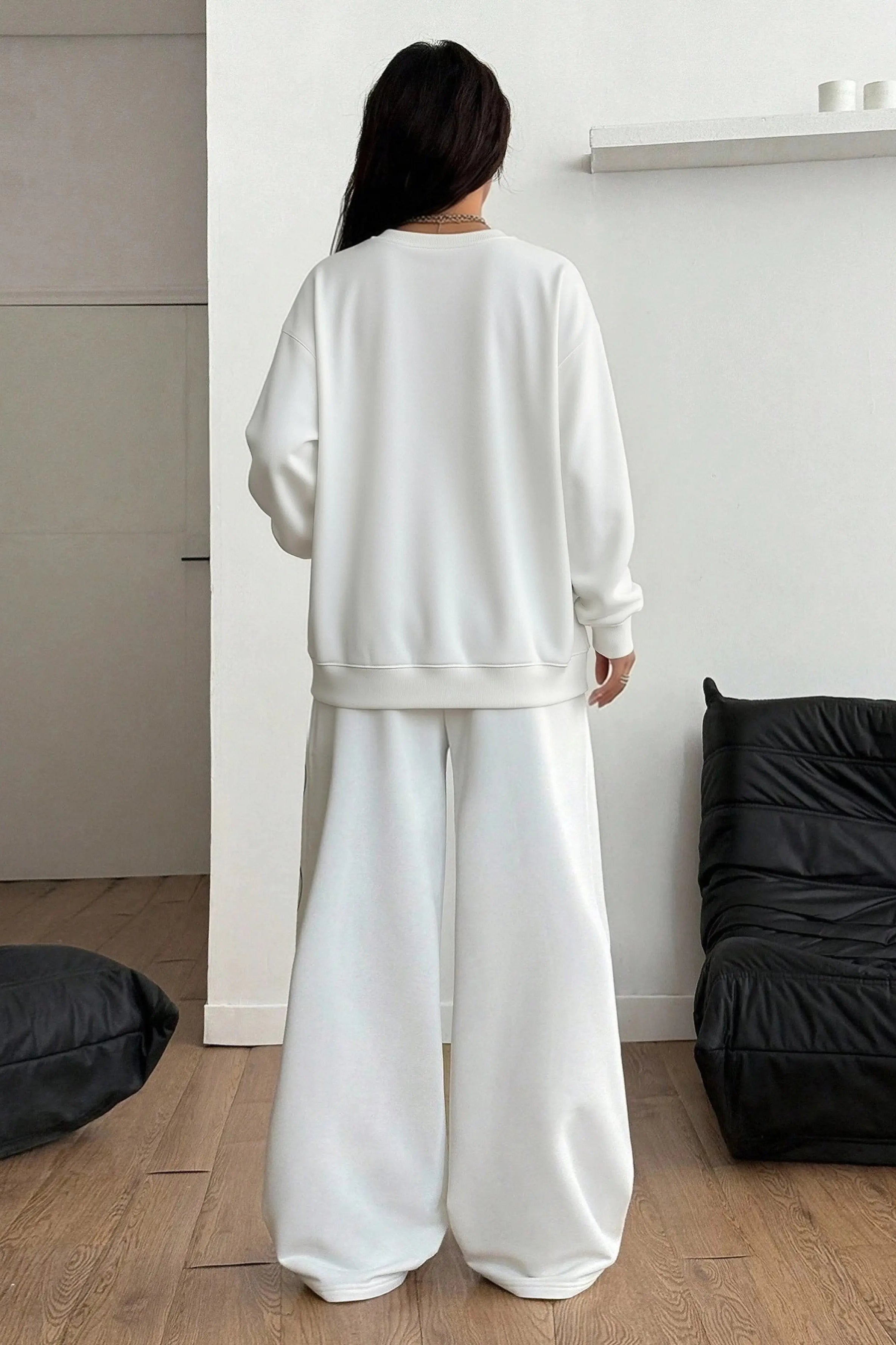 Person wearing a white outfit standing in a minimalistic room with black furniture. TCH BOY LONDON Rhinestone Logo Print Crew Neck Sweatshirt