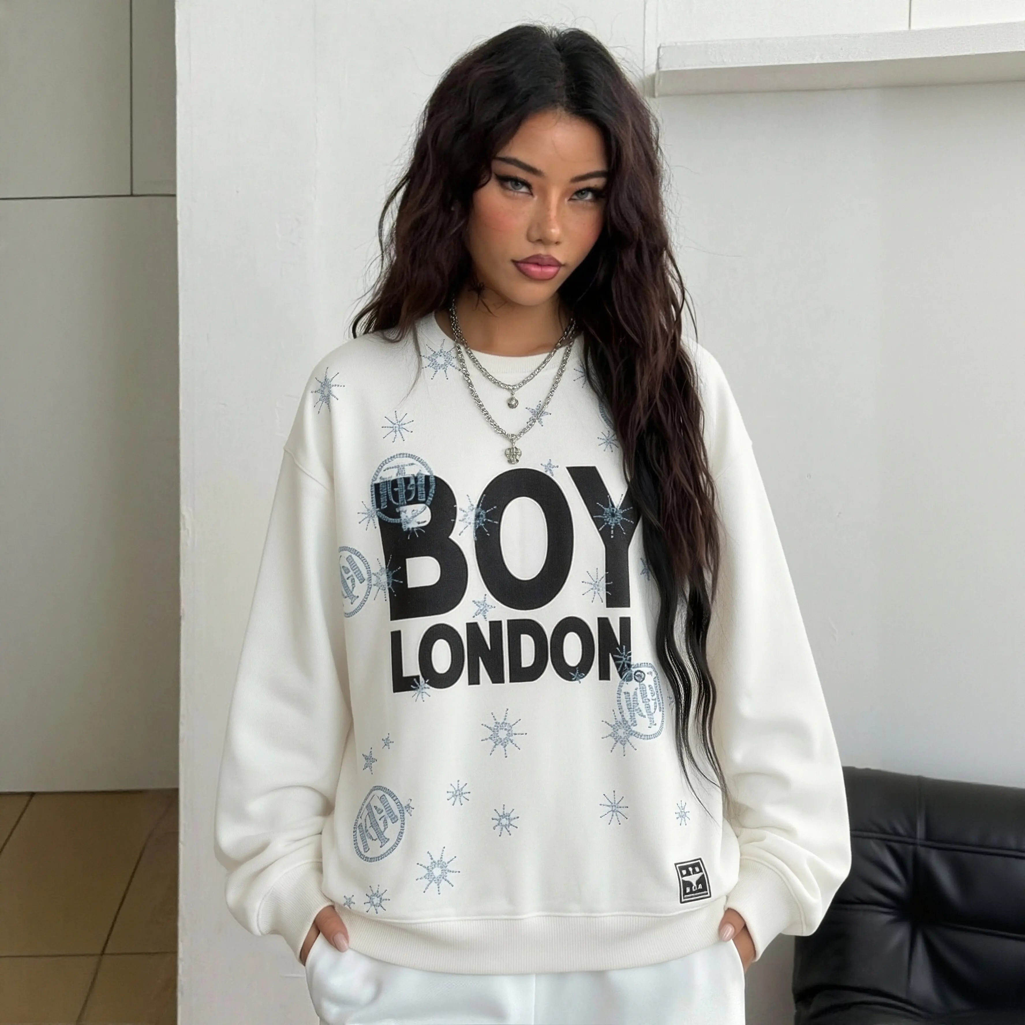Woman wearing a white sweatshirt with 'BOY LONDON' text in a modern indoor setting, TCH BOY LONDON Rhinestone Logo Print Crew Neck Sweatshirt