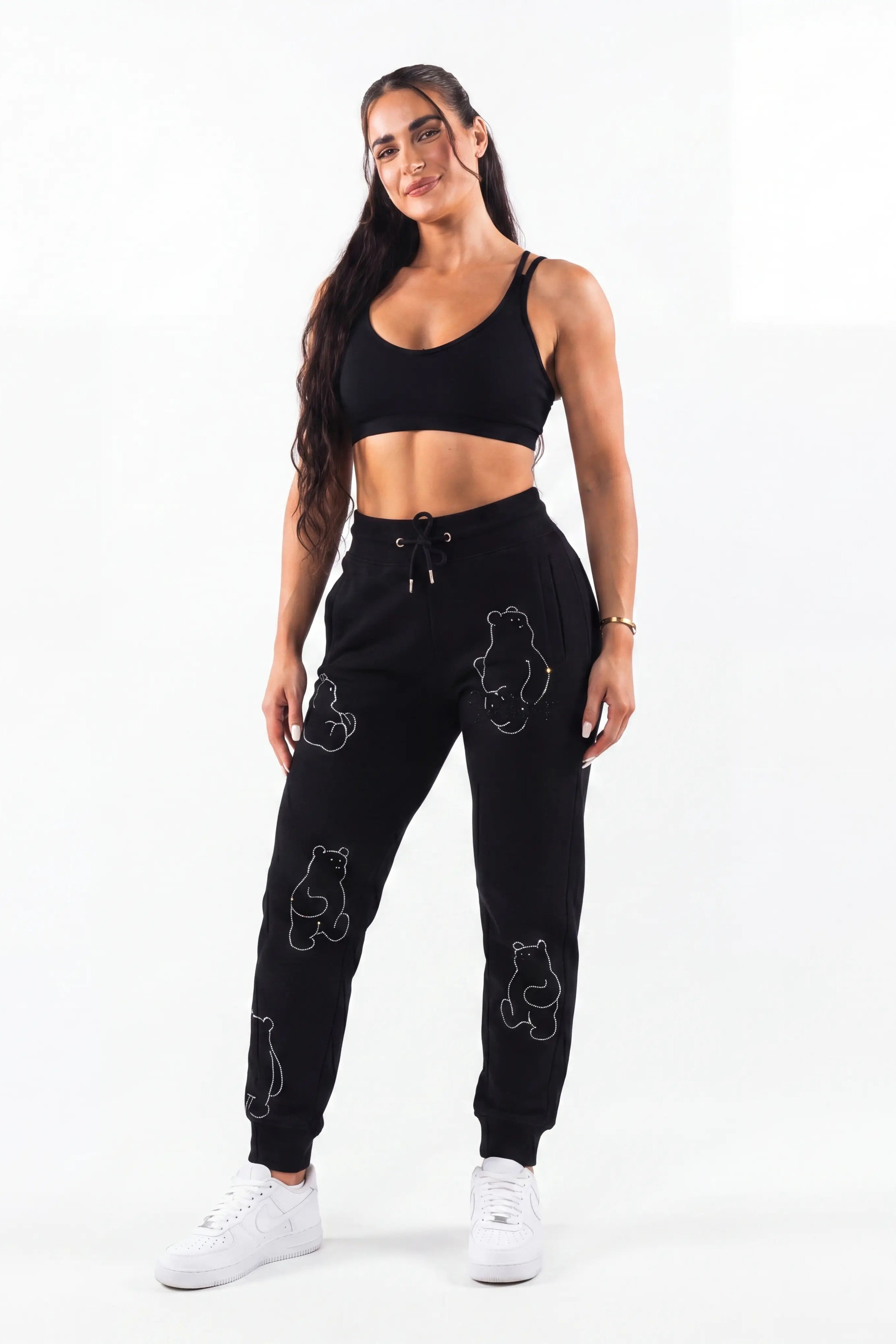 Woman wearing a black athletic outfit with bear designs on a white background, TCH Bear Sketch Rhinestone Jogger Pants