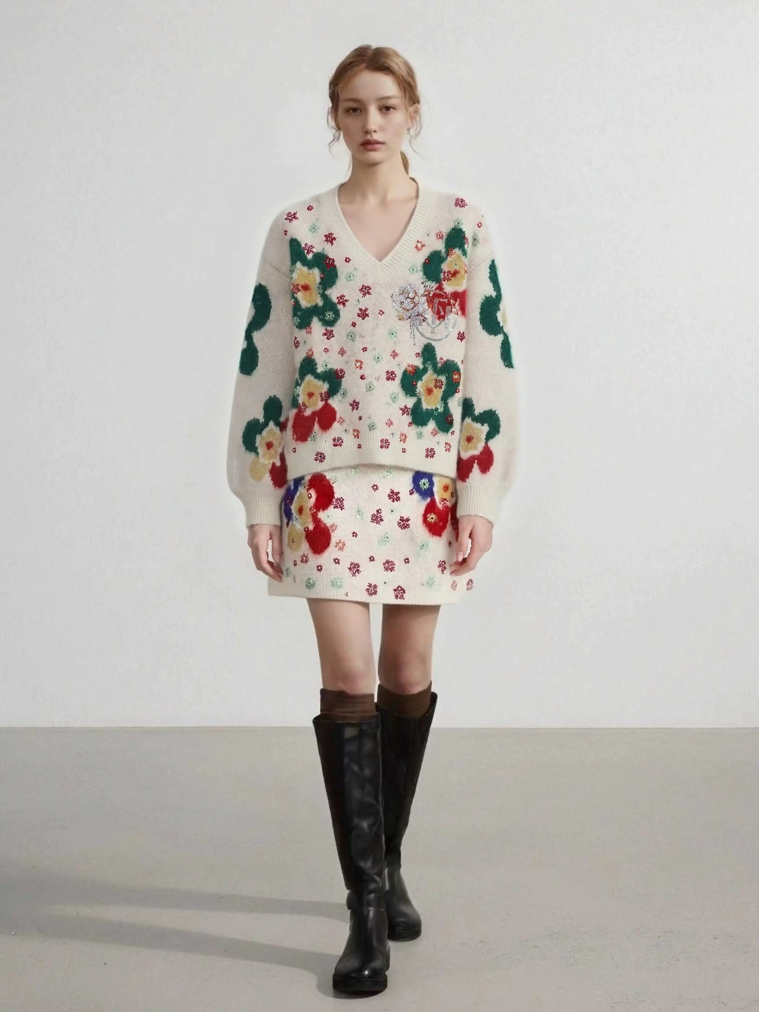 Woman wearing a floral dress with a sweater over it and black knee-high boots on a plain background, TCH Beige Floral Rhinestone V-Neck Sweater & Wool Mini Skirt Set