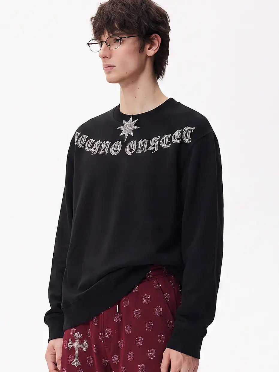 A man wearing a black crewneck sweatshirt with 'TECHNO OUTLET' in a gothic font and a silver star graphic on the chest, paired with burgundy patterned pants, against a plain white background. TCH Black Old English Techno Graphic Sweatshirt