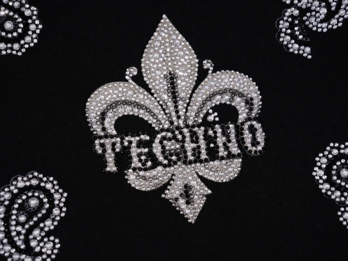 A close-up of a black fabric featuring a large silver fleur-de-lis embellished with rhinestones and the word 'TECHNO' across the center, with smaller matching rhinestone patterns in the corners. TCH Black Paisley Print Wide-Leg Sweatpants