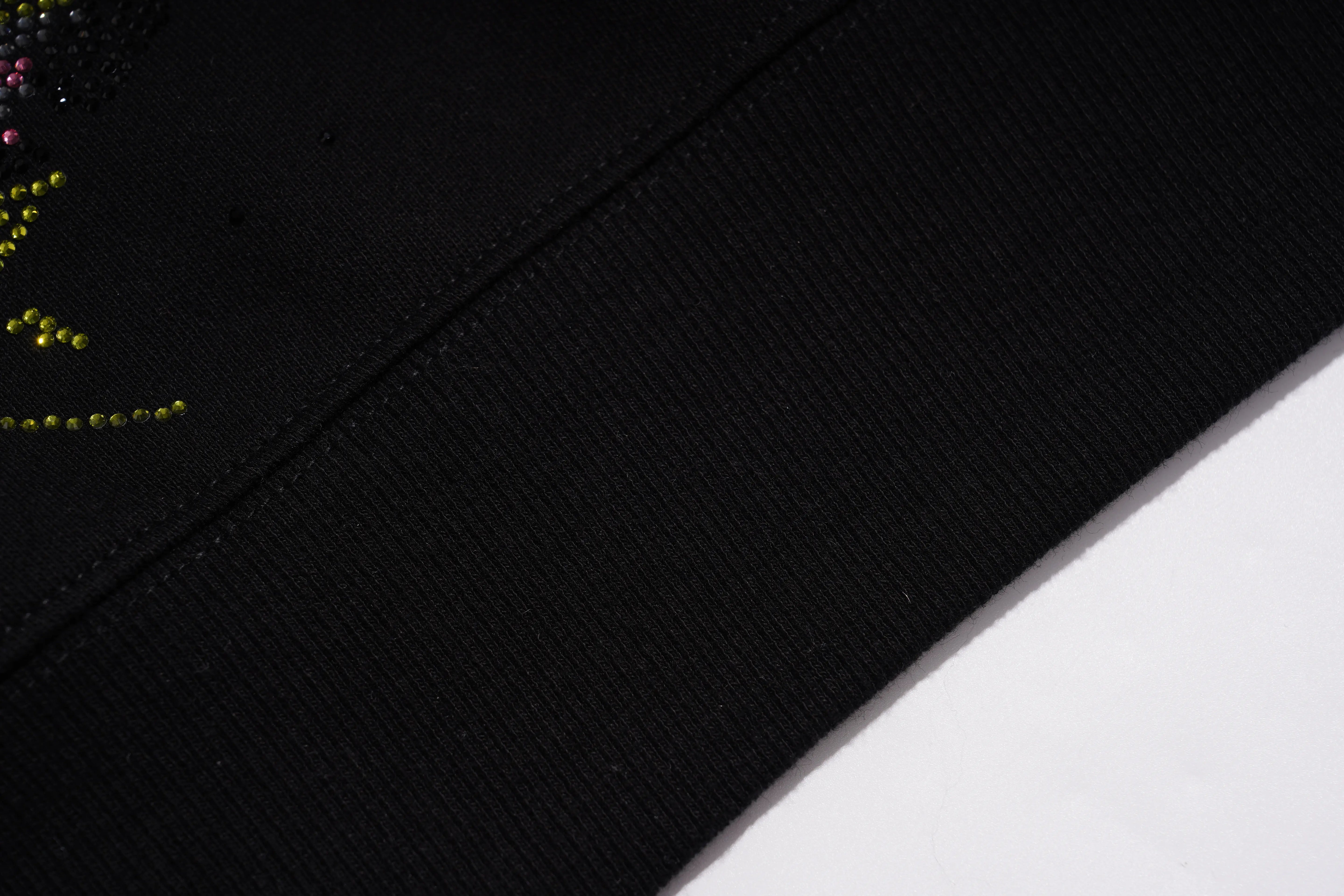 Close-up detail of a black ribbed knit garment, showing a diagonal seam and a small section of multicolor rhinestone embellishment on the upper left. TCH Black Panda Rhinestone Sweatshirt