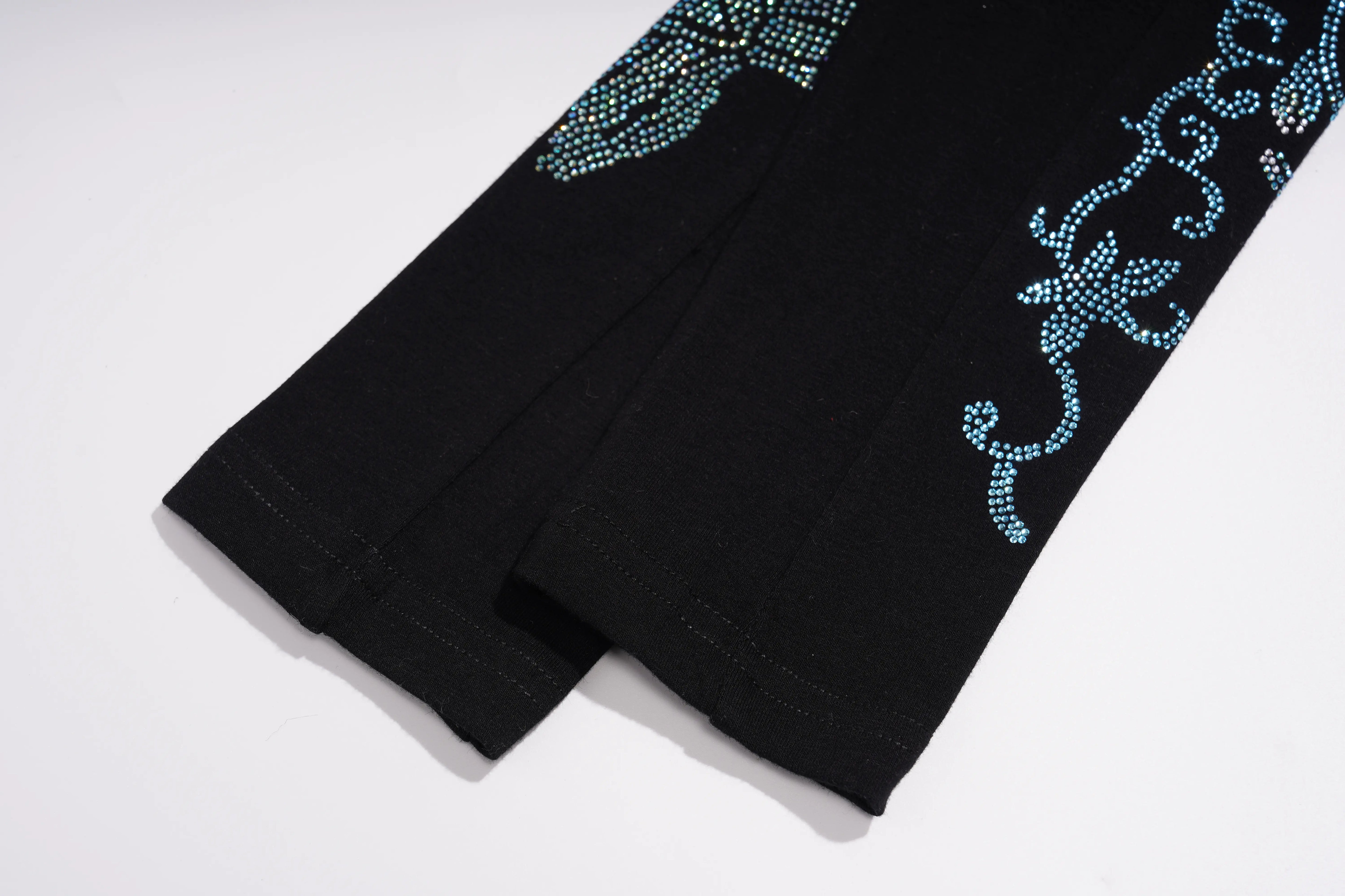 Close-up of a black garment laid flat on a white background, showing decorative turquoise rhinestone floral embroidery along the side. TCH Black Rhinestone Floral Leggings