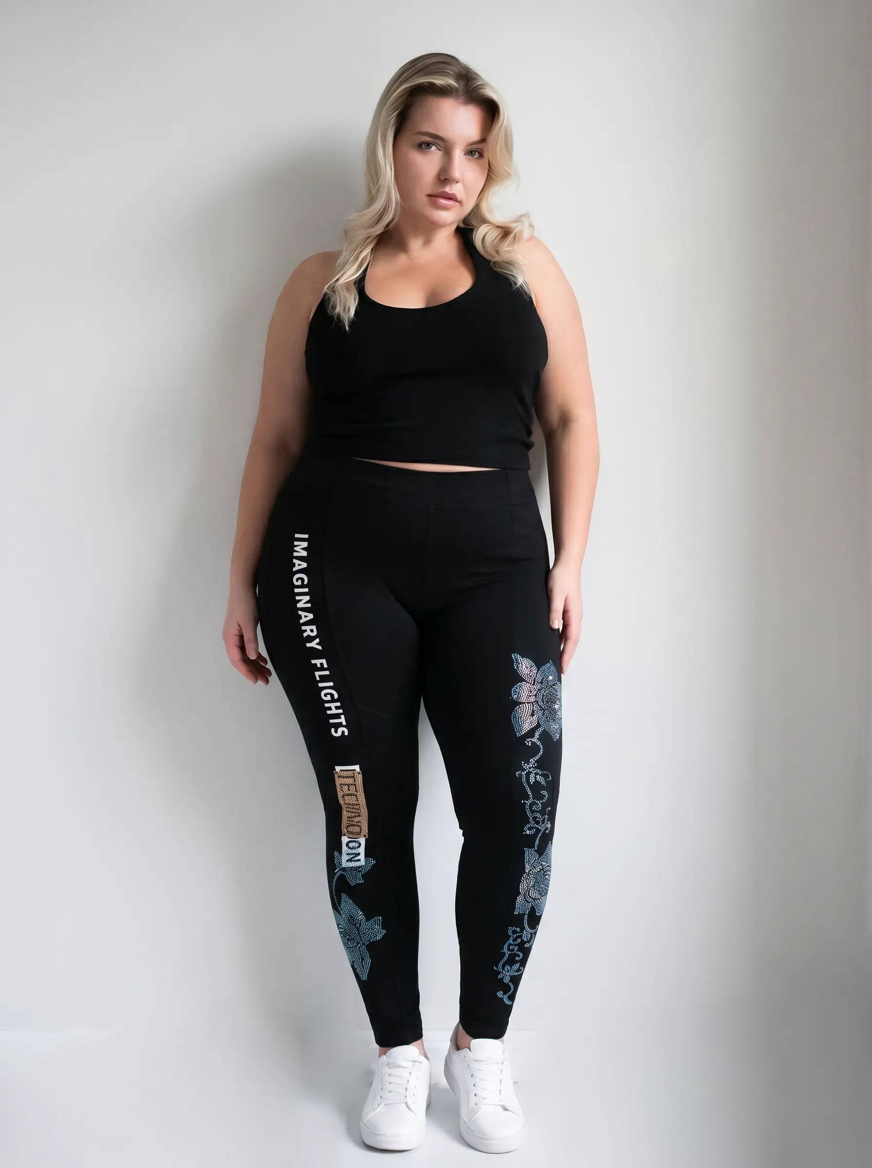A woman modeling black activewear leggings with white text and blue butterfly graphics, paired with a black crop top and white sneakers, against a light gray studio background. TCH Black Rhinestone Floral Leggings