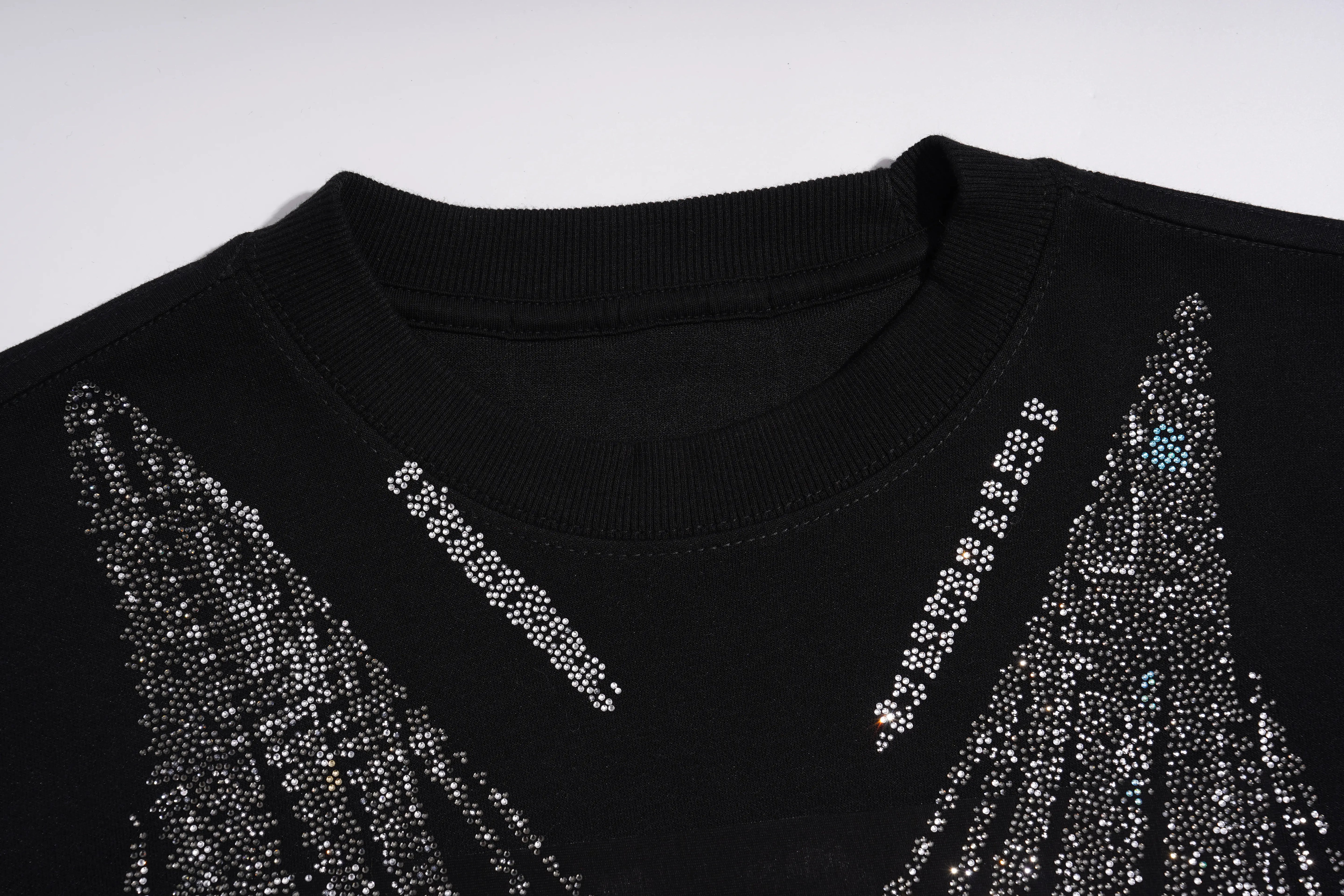 Close-up of a black crewneck sweater decorated with sparkling silver rhinestones forming wing-like patterns on the shoulders, set against a plain light gray background. TCH Black Rhinestone Fringe Detail Long Sleeve Mini Dress