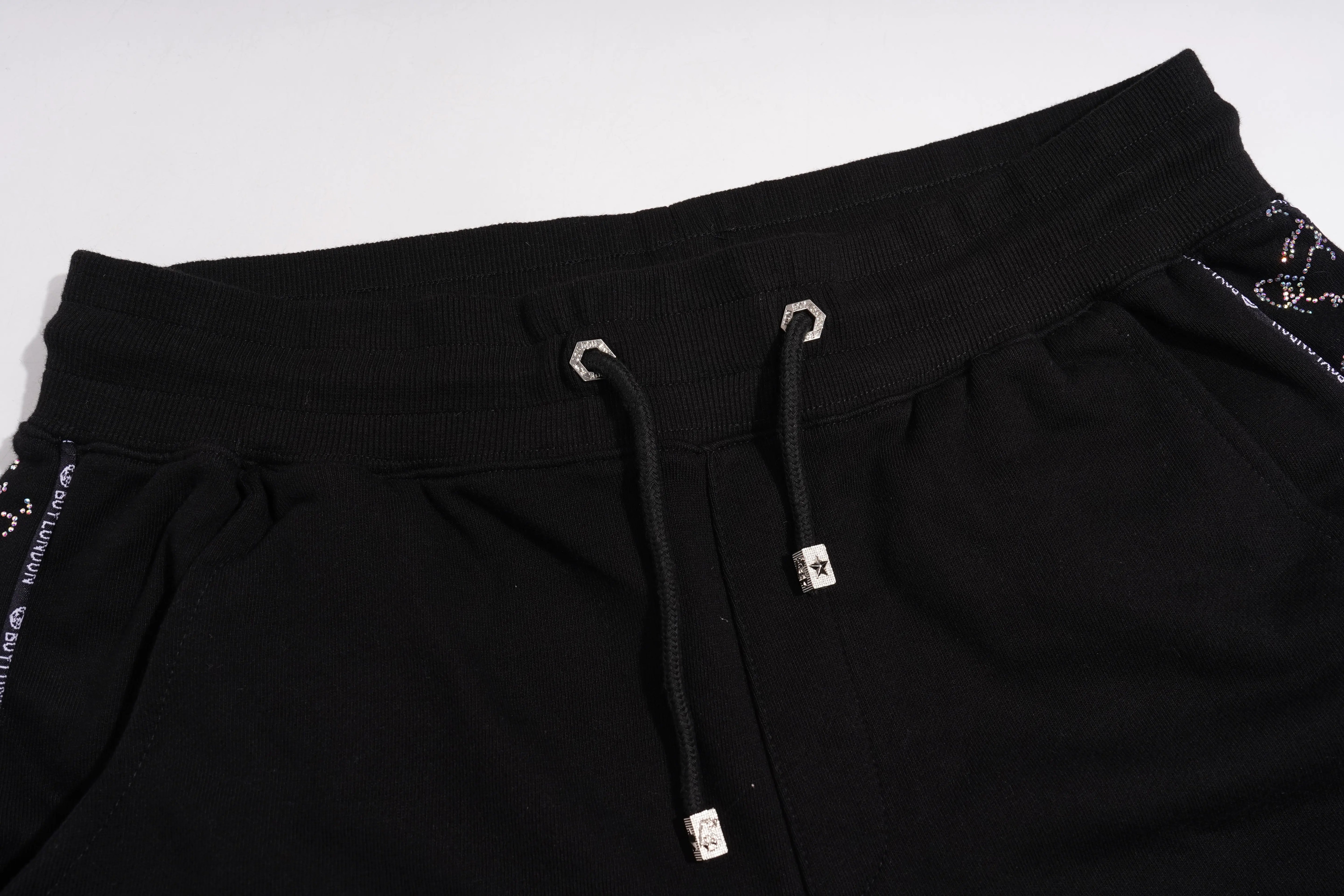 Close-up of black pants with drawstring and brand logo on a white background, TCH Black Rhinestone Side Stripe Jogger Pants