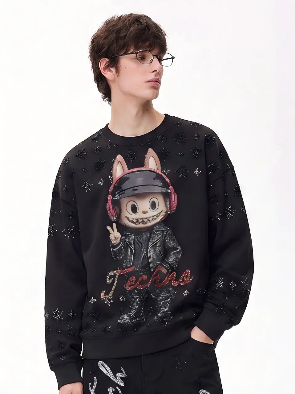 A man wearing a black crewneck sweatshirt with a graphic of a cartoon character in a black leather jacket and pink headphones, with the word 'Techno' written below, set against a plain white background. TCH Black Techno Bunny Rhinestone Graphic Sweatshirt