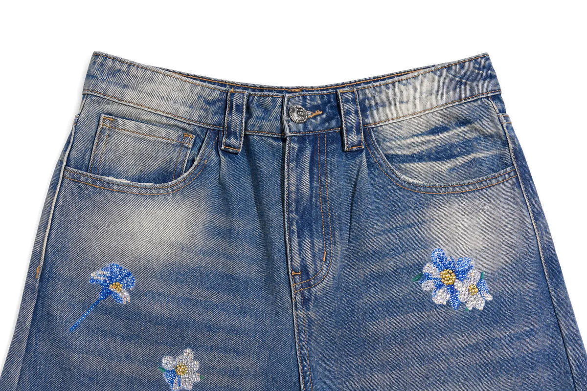 Close-up of a blue denim skirt with a faded wash and embroidered blue and white daisy details on the front. TCH Blue Floral Rhinestone Wide-Leg Jeans