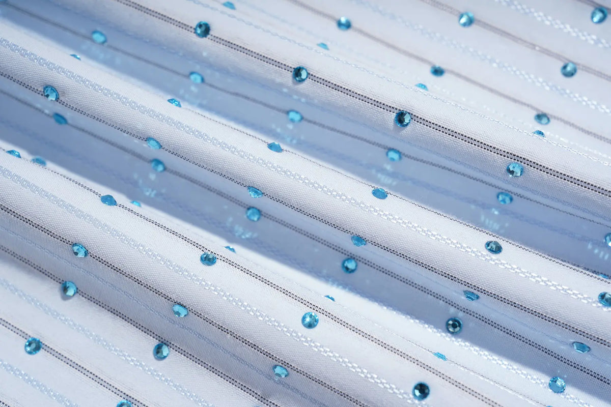 A close-up of a white tulle fabric with diagonal rows of small, shiny light blue rhinestones. TCH Blue Striped Tie Detail Button-Up Shirt