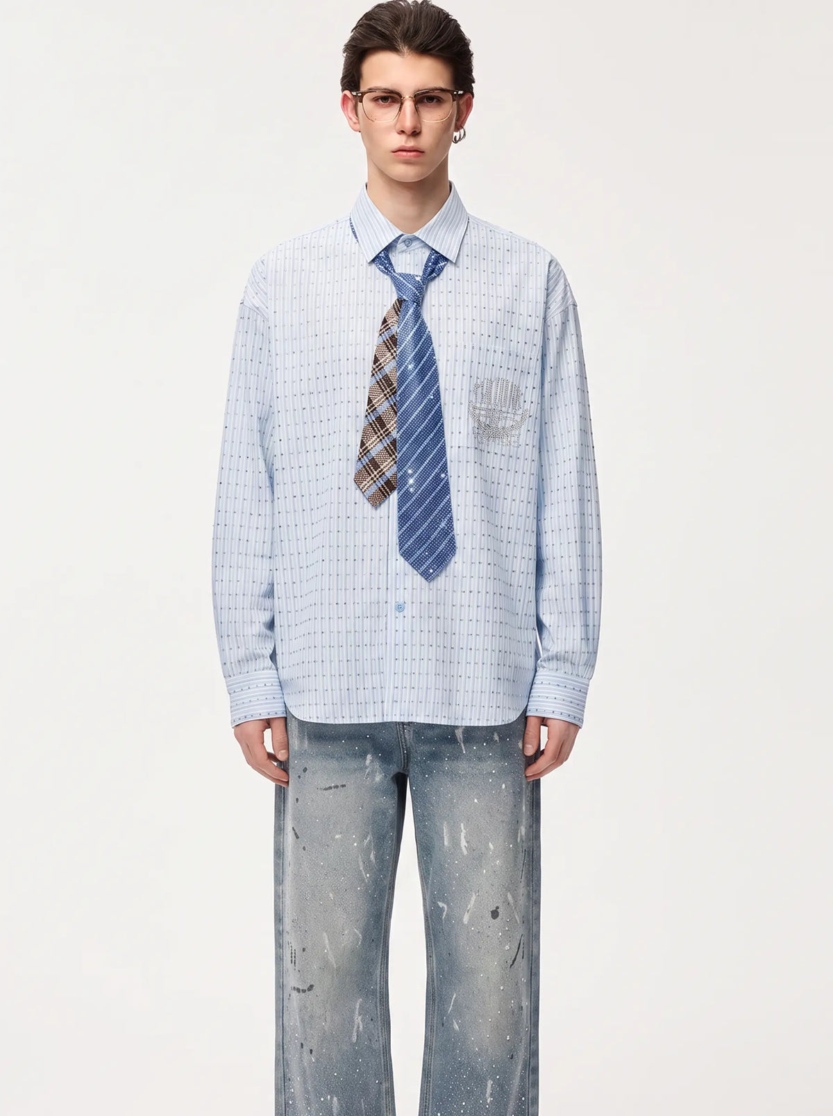 A male model wearing a light blue and white checkered long-sleeve button-down shirt, a blue striped tie, and distressed blue jeans, standing against a plain off-white studio background. TCH Blue Striped Tie Detail Button-Up Shirt