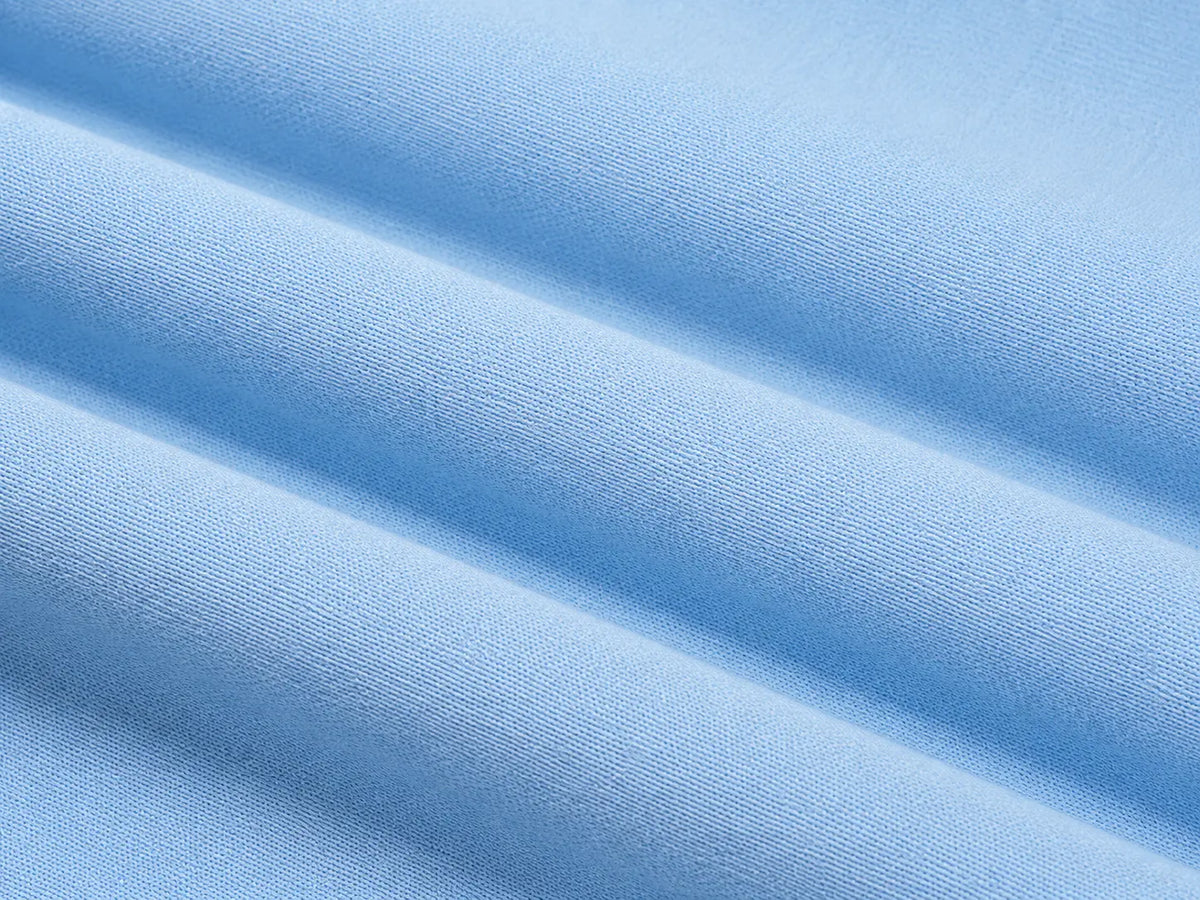 A close-up of light blue fabric with soft diagonal folds showing a fine woven texture. TCH Blue Teddy Bear Floral Rhinestone Hoodie