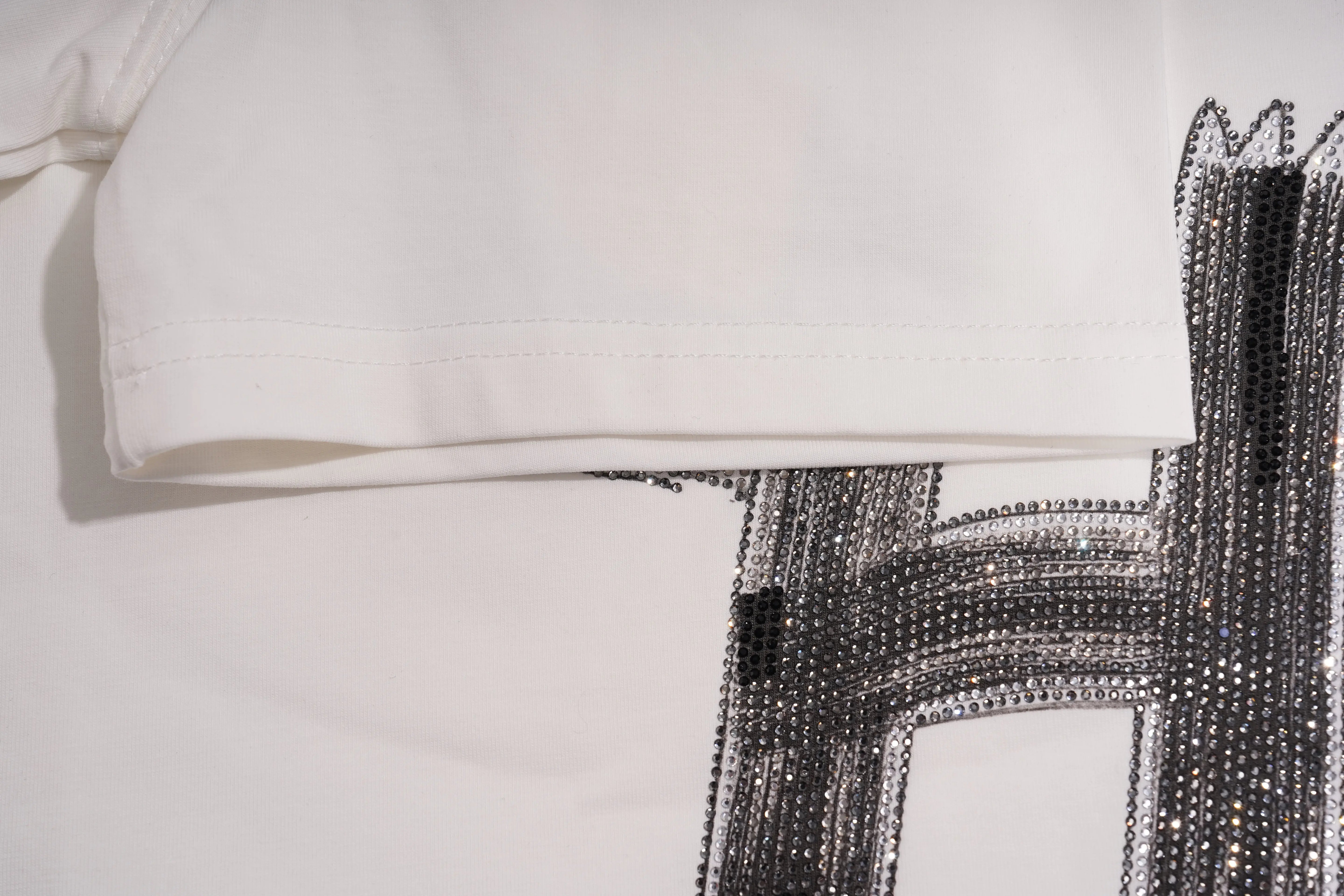 A close-up of a white fabric embellished with dense rhinestone floral embroidery, featuring blue, green, and brown tones with a central red accent. TCH Brush Logo Graphic Oversized T-Shirt