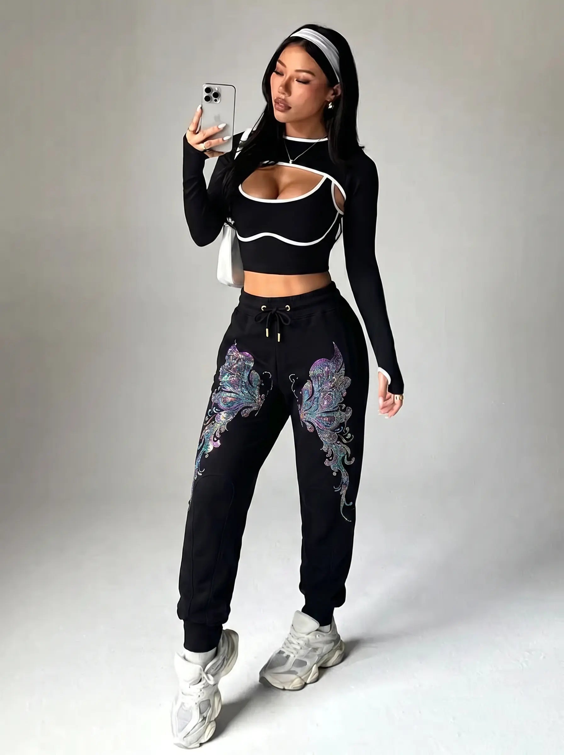 A woman modeling a black two-piece activewear set with white trim and purple butterfly graphics on the sweatpants, taking a mirror selfie against a light gray studio background. TCH Butterfly Rhinestone Graphic Black Jogger Pants