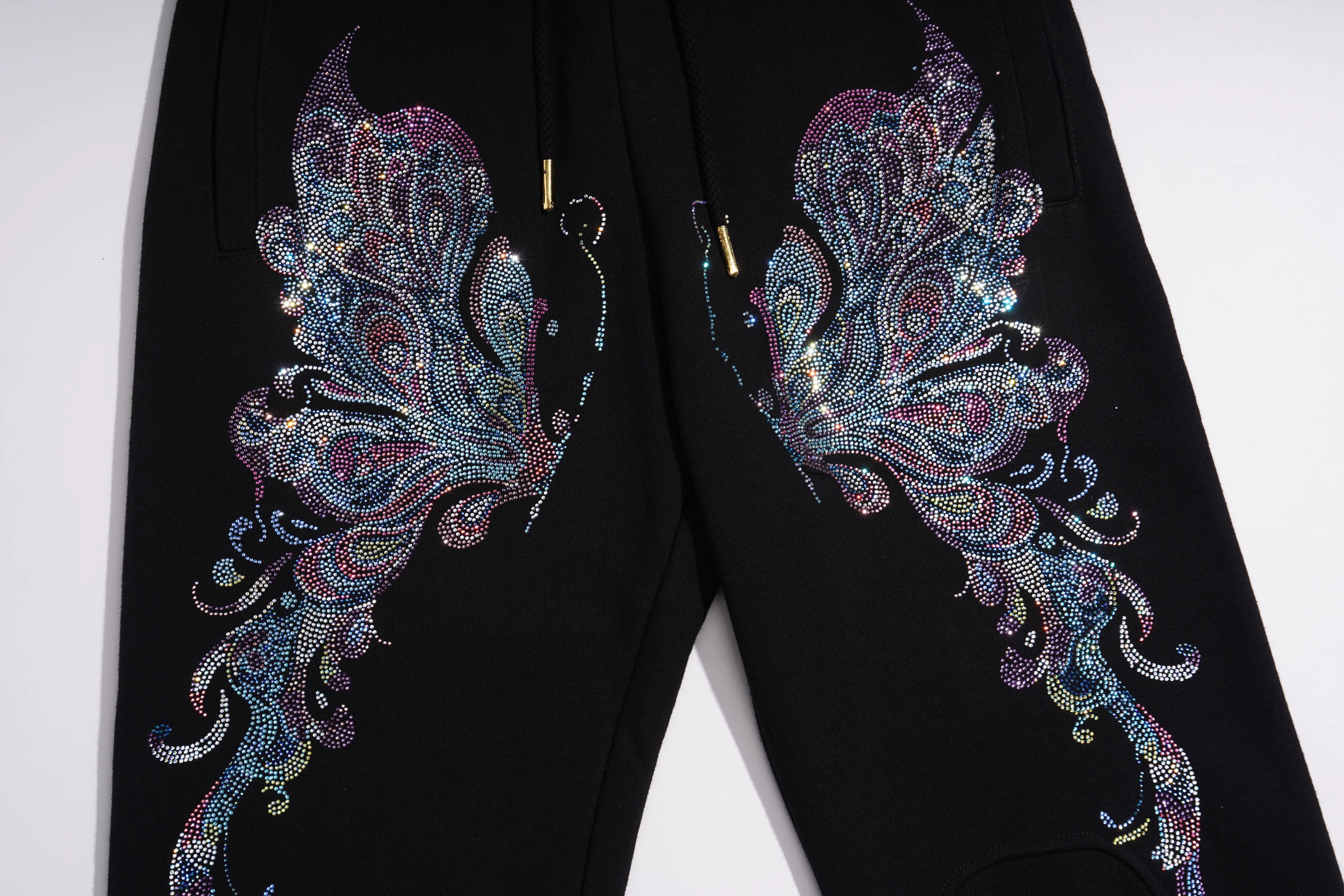 Black pants featuring large, ornate iridescent butterfly wing designs on both legs, embellished with sequins and glitter, shown against a plain white background. TCH Butterfly Rhinestone Graphic Black Jogger Pants