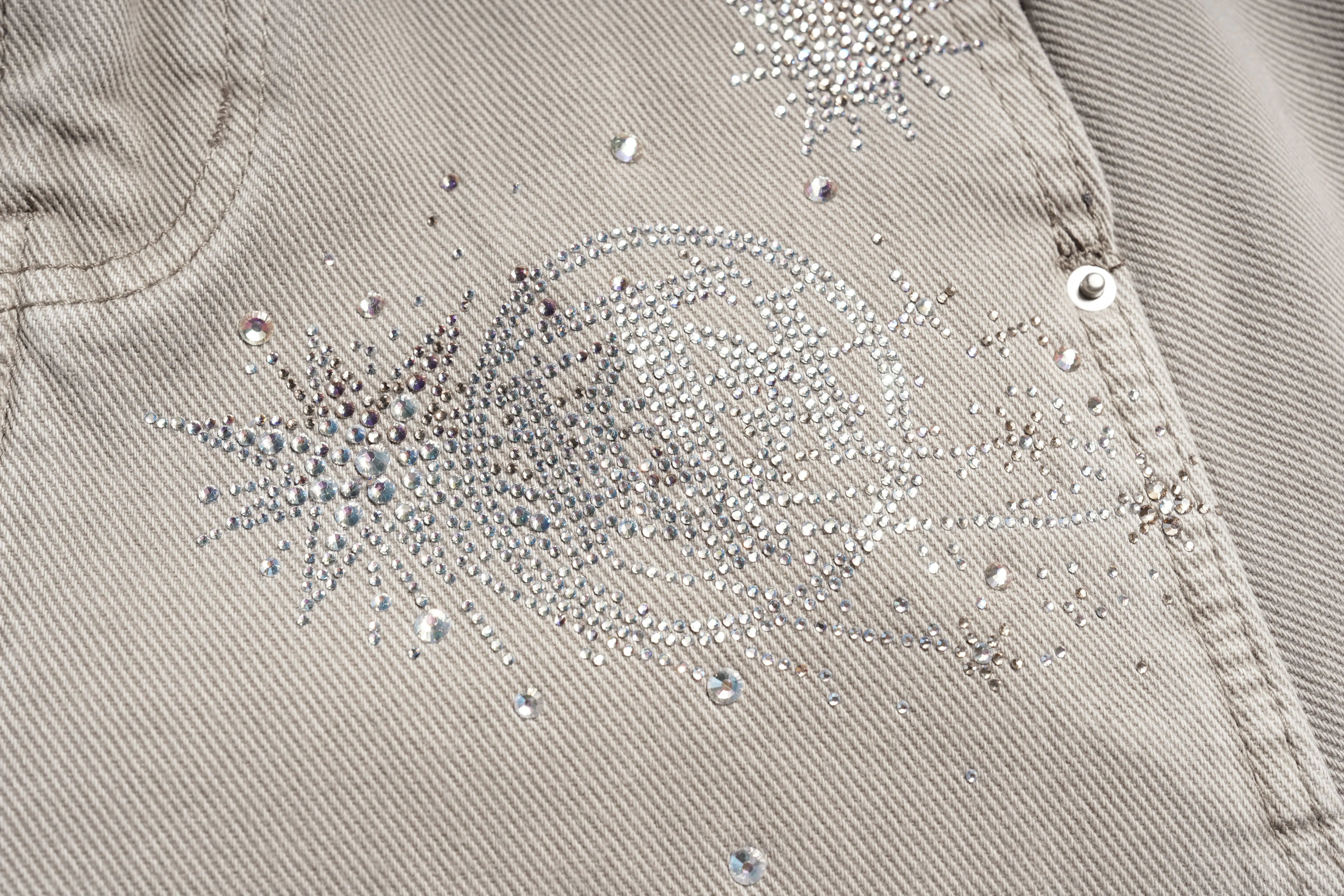 Close-up of a beige fabric with decorative crystal embellishments. TCH Celestial Firework Rhinestone Wide-Leg Pants
