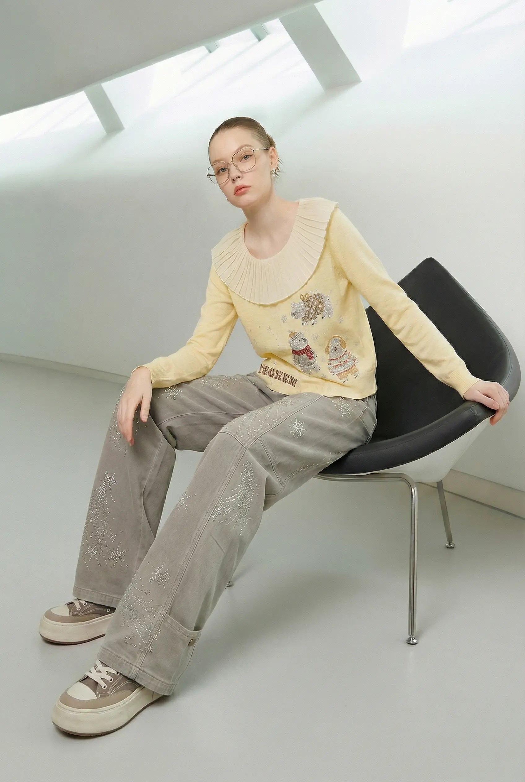 Person sitting on a modern chair wearing a yellow sweater and gray pants in a minimalistic room. TCH Celestial Firework Rhinestone Wide-Leg Pants