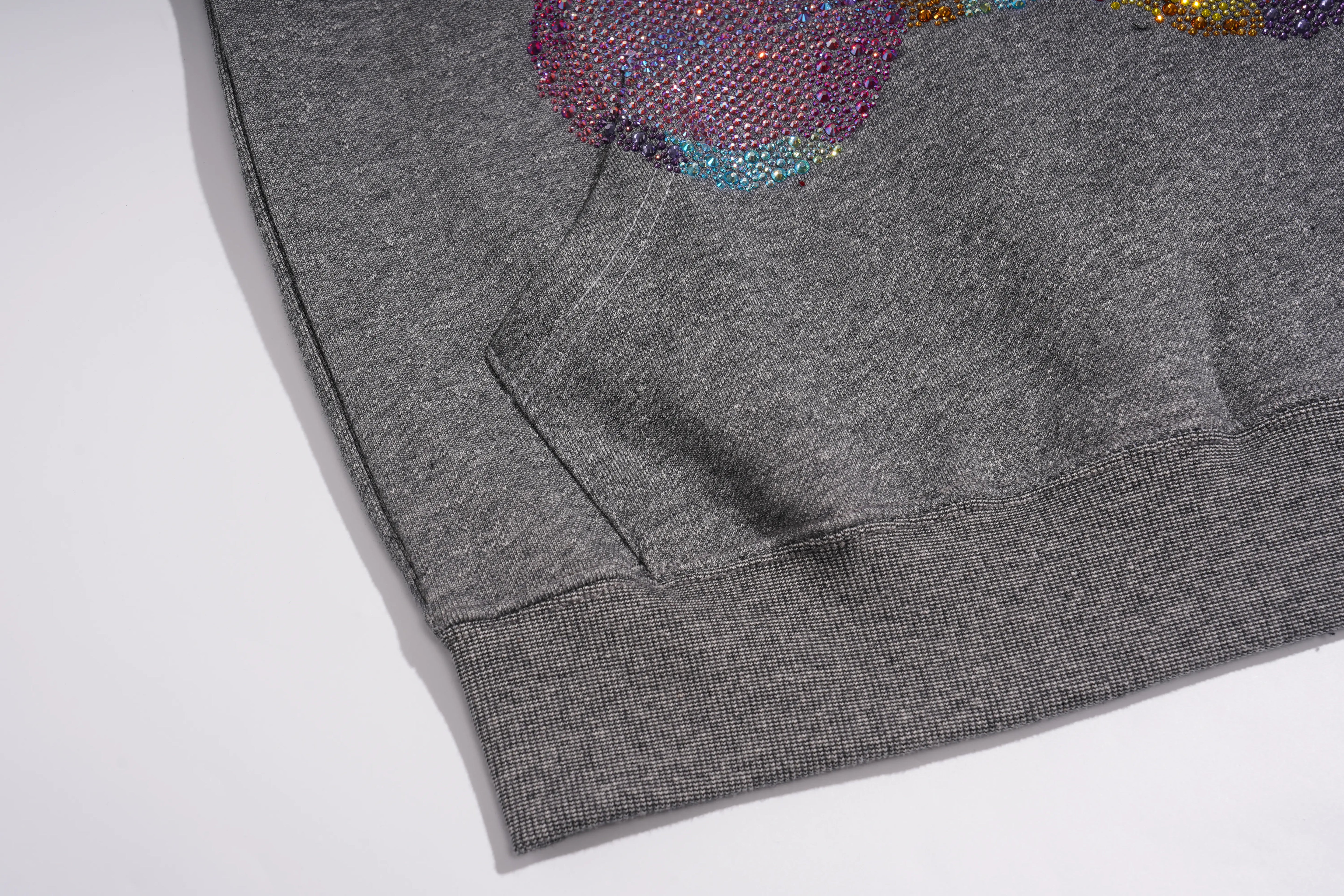 Close-up of a heather gray ribbed knit garment, showing the sleeve cuff, pocket seam, and part of a colorful sequined graphic on a white background. TCH Colorful Rhinestone Teddy Bear Crewneck Sweatshirt
