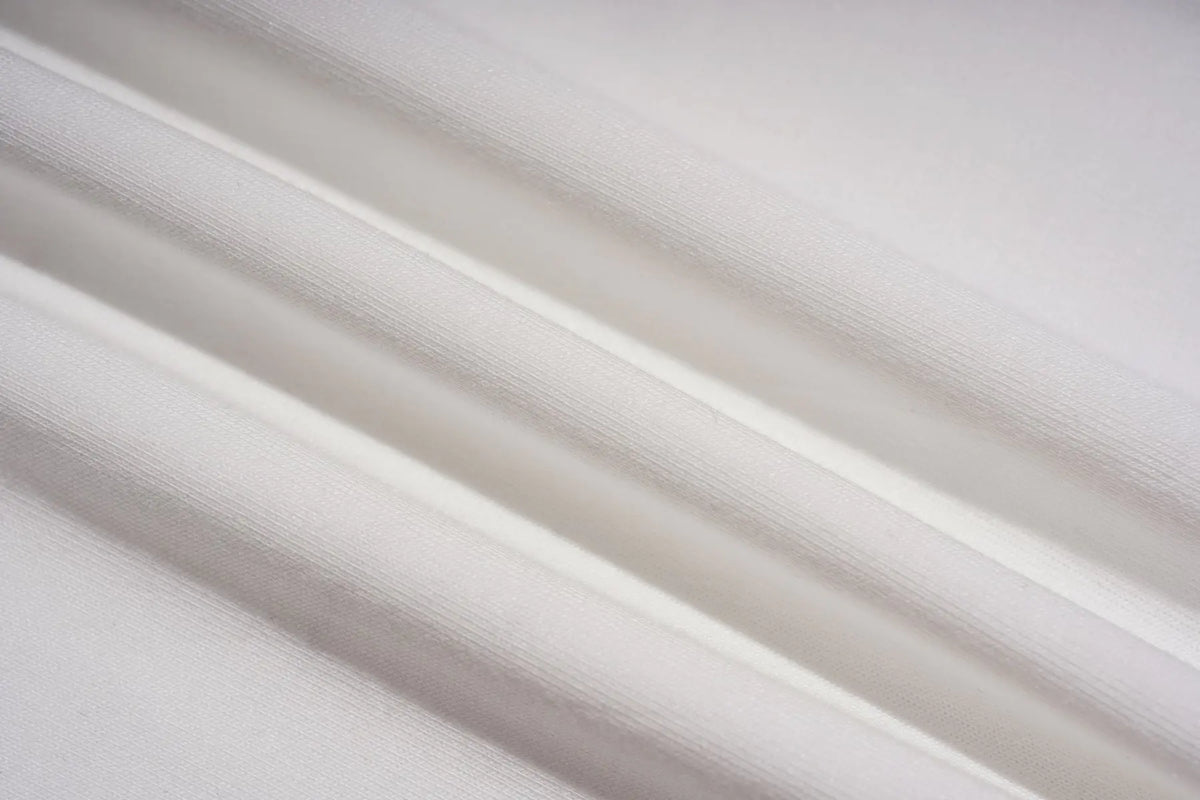 A close-up of draped white fabric with soft diagonal folds and a fine woven texture. TCH Crystal Bear Graphic Wide-Leg Sweatpants