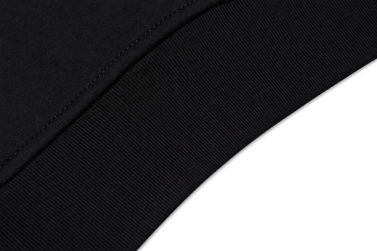 Close-up of a black ribbed fabric trim with fine stitching along a curved edge against a white background. TCH Crystal Wing Graphic Zip Up Hoodie