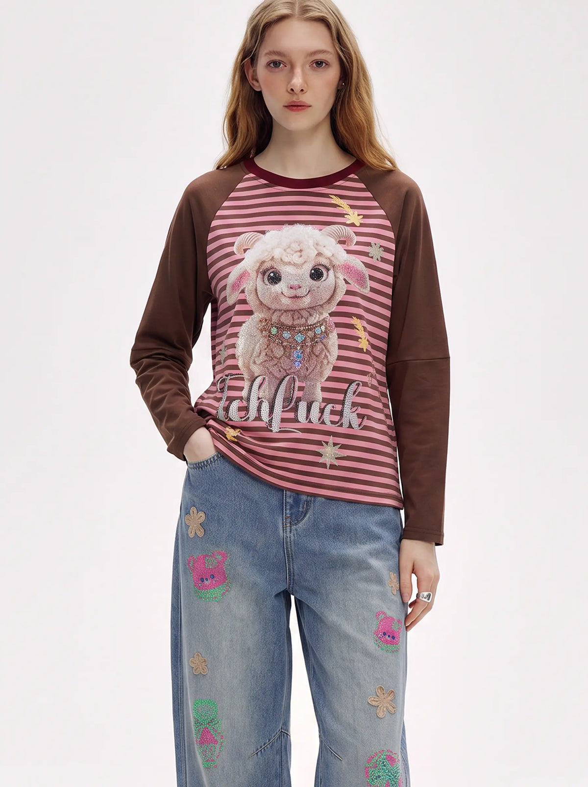 A model wearing a long-sleeve raglan t-shirt with a pink and red striped body, brown sleeves, and a graphic of a sheep on the front, paired with light blue jeans decorated with small colorful patches. TCH Cute Lamb Pink Striped Raglan Long Sleeve Top
