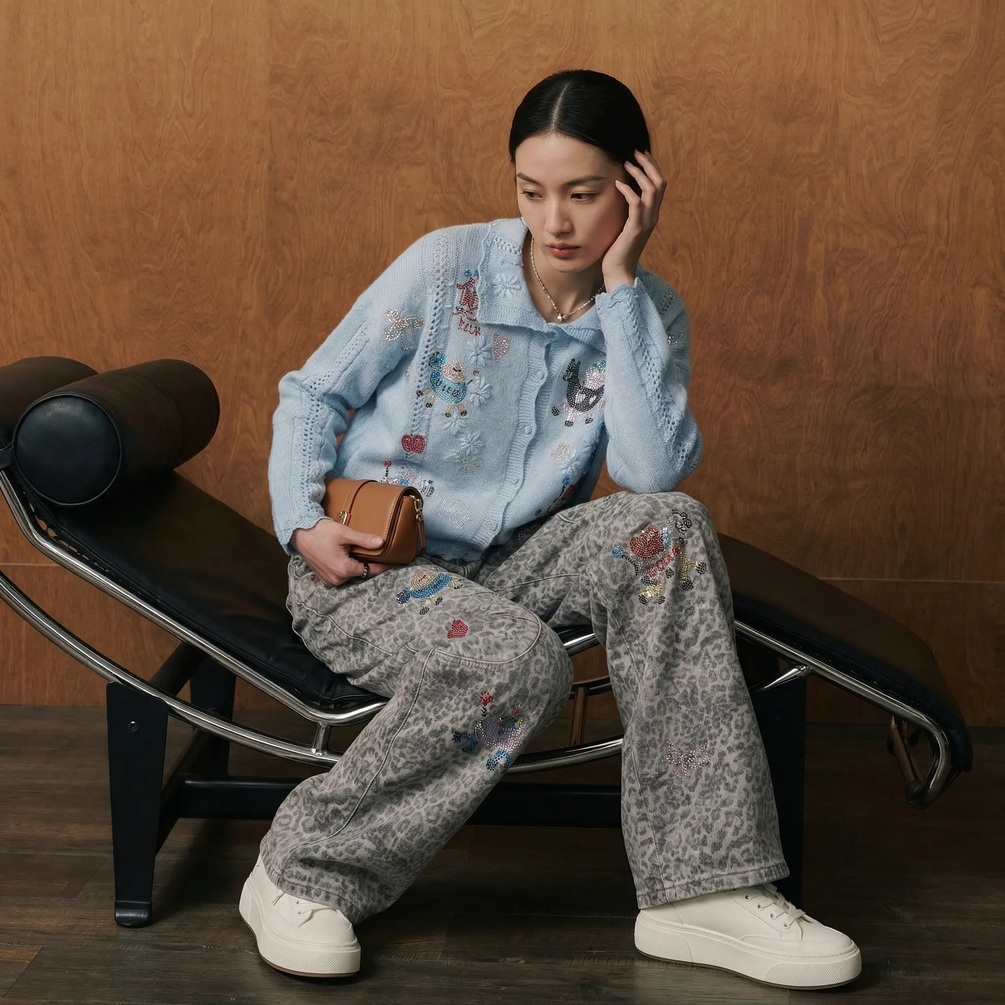 Woman sitting on a black lounge chair wearing a light blue embroidered jacket and gray patterned pants. TCH Cute Pony Rhinestone Grey Leopard Wide-Leg Jeans