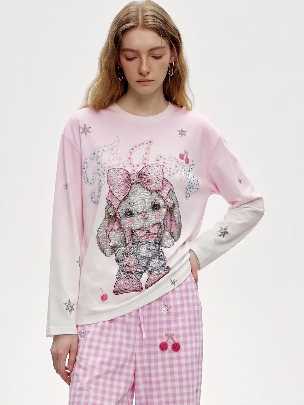 A model wearing a light pink long-sleeve pajama top with a cute bunny graphic and pink gingham pants against a plain white studio background. TCH Cute Rhinestone Cat Graphic Pink Long Sleeve T-Shirt