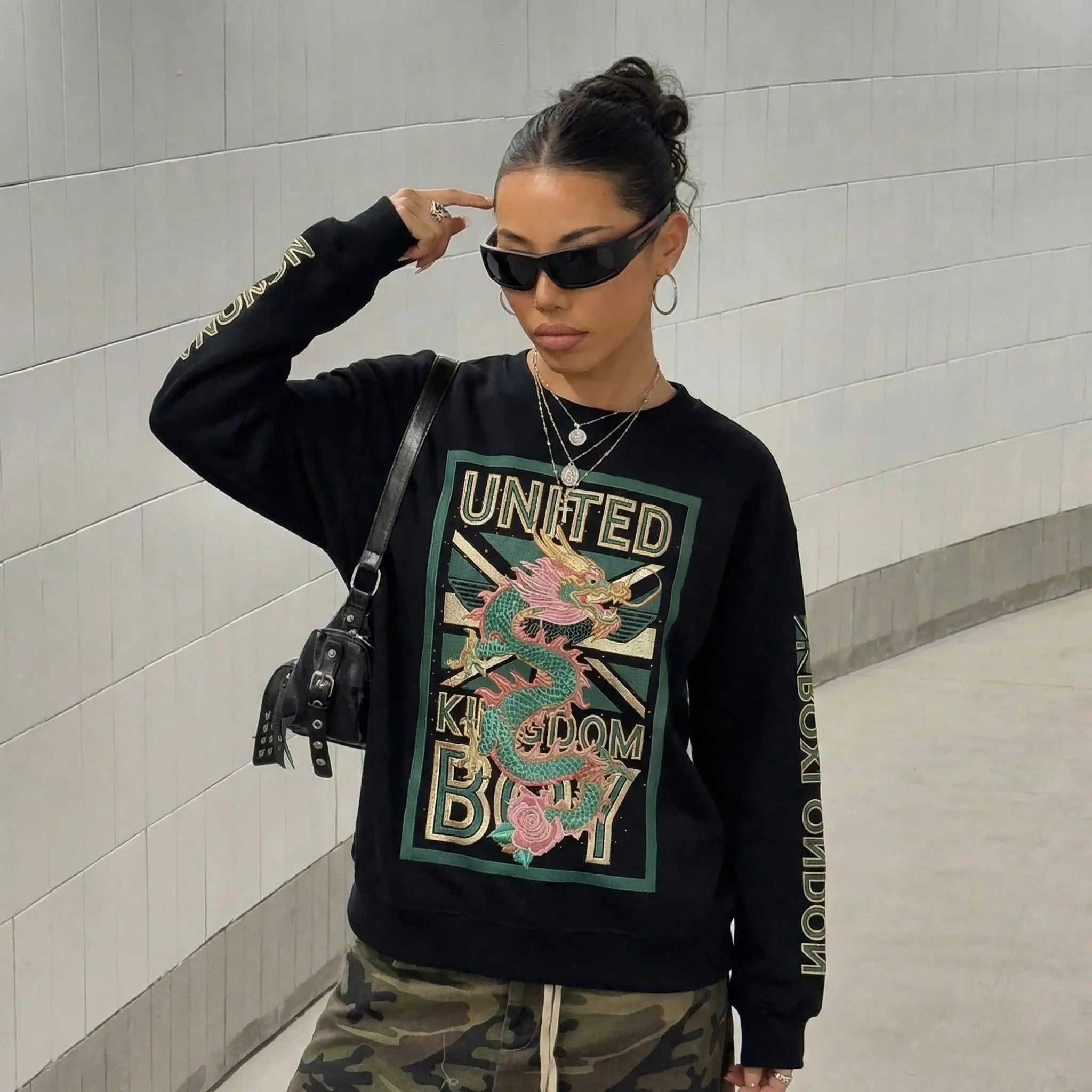 Person wearing a black sweatshirt with a colorful graphic design and text, standing against a light gray wall. TCH Dragon Embroidered Rhinestone Sweatshirt-