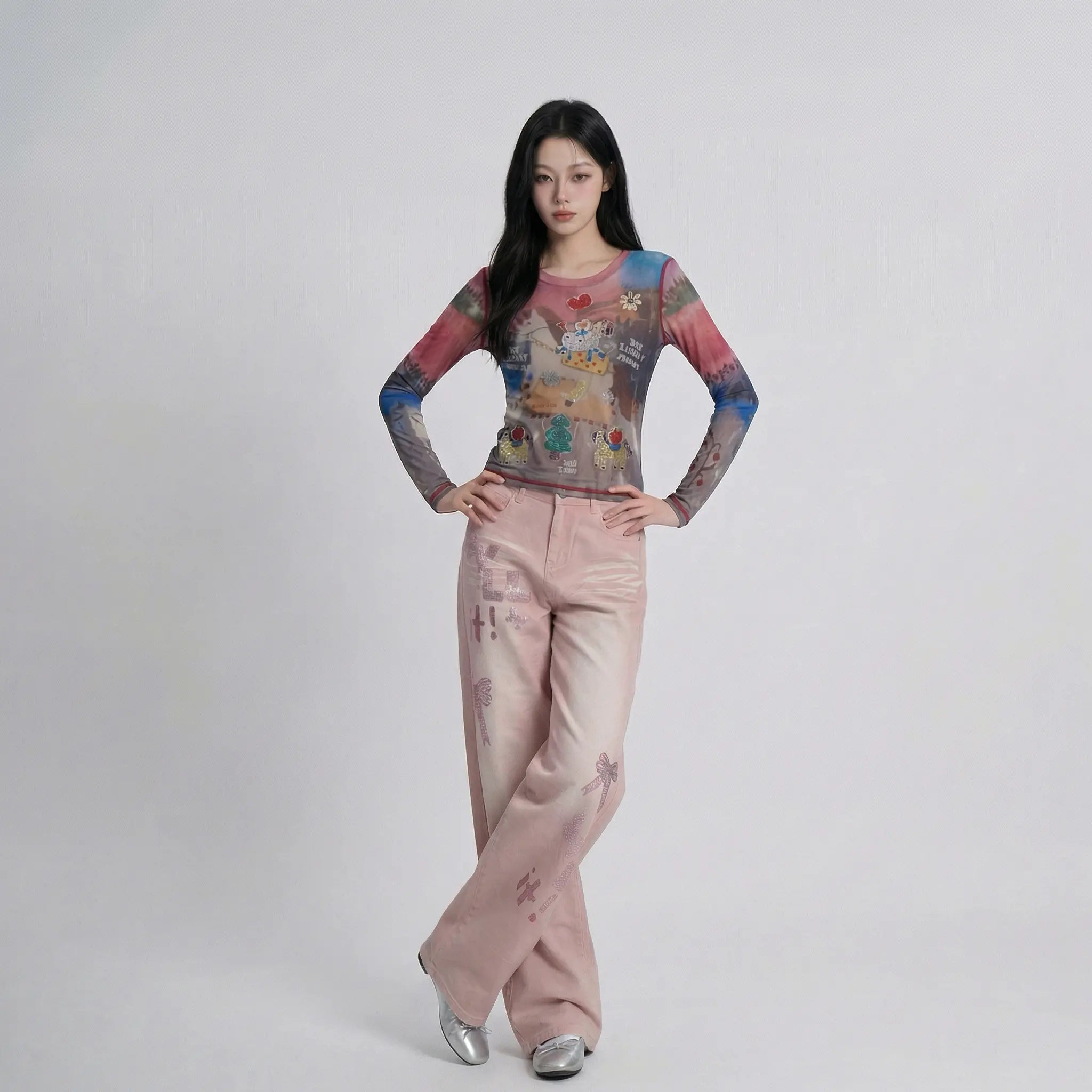 A woman modeling a long-sleeve crewneck top with a colorful, painterly graphic print and matching wide-leg pink pants with subtle tonal prints, standing against a light gray studio background. TCH Dream Garden Rhinestone Mesh Long Sleeve Top