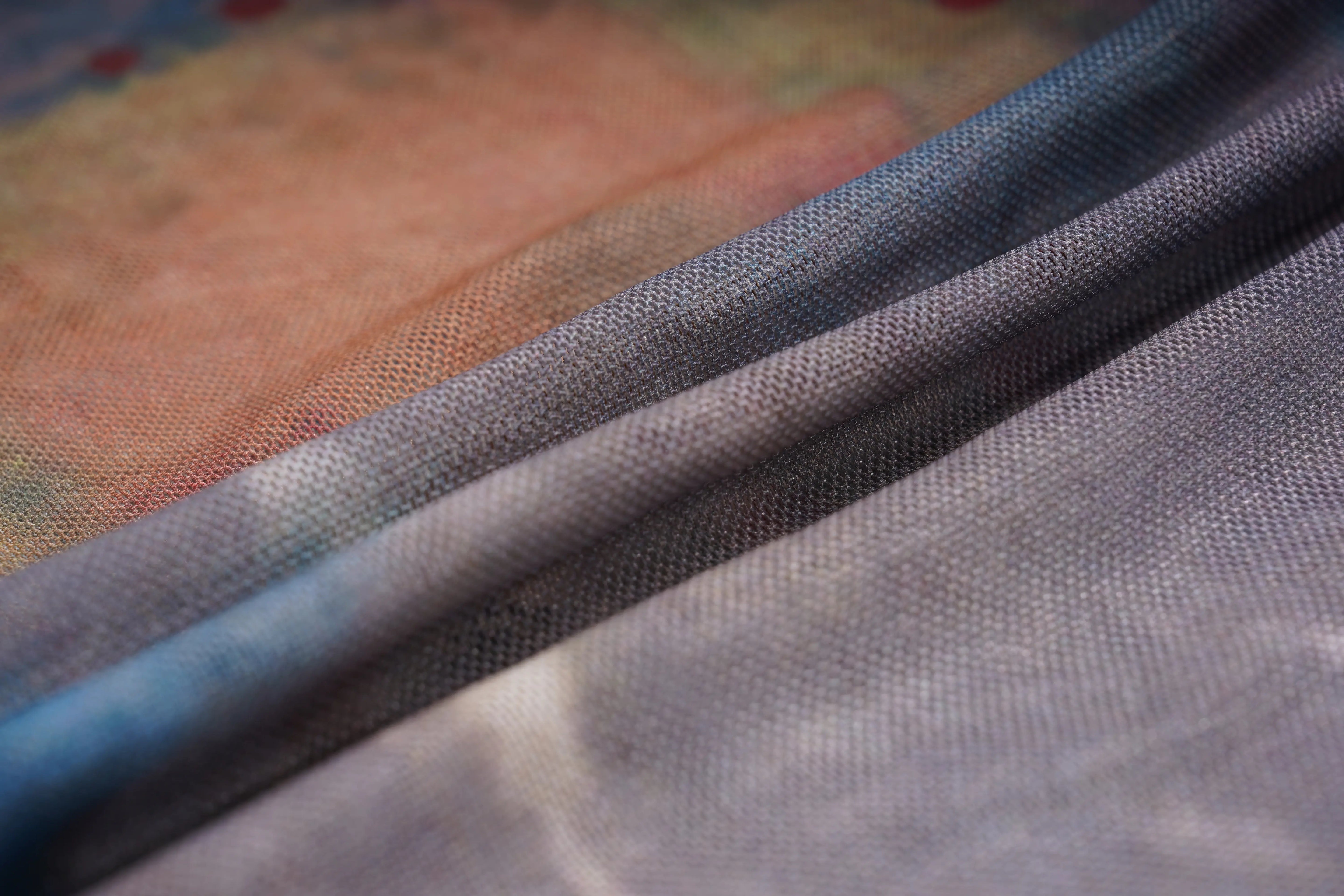 Close-up of a sheer mesh fabric with a blue-to-gray gradient, layered over a soft peach-colored textured fabric. TCH Dream Garden Rhinestone Mesh Long Sleeve Top