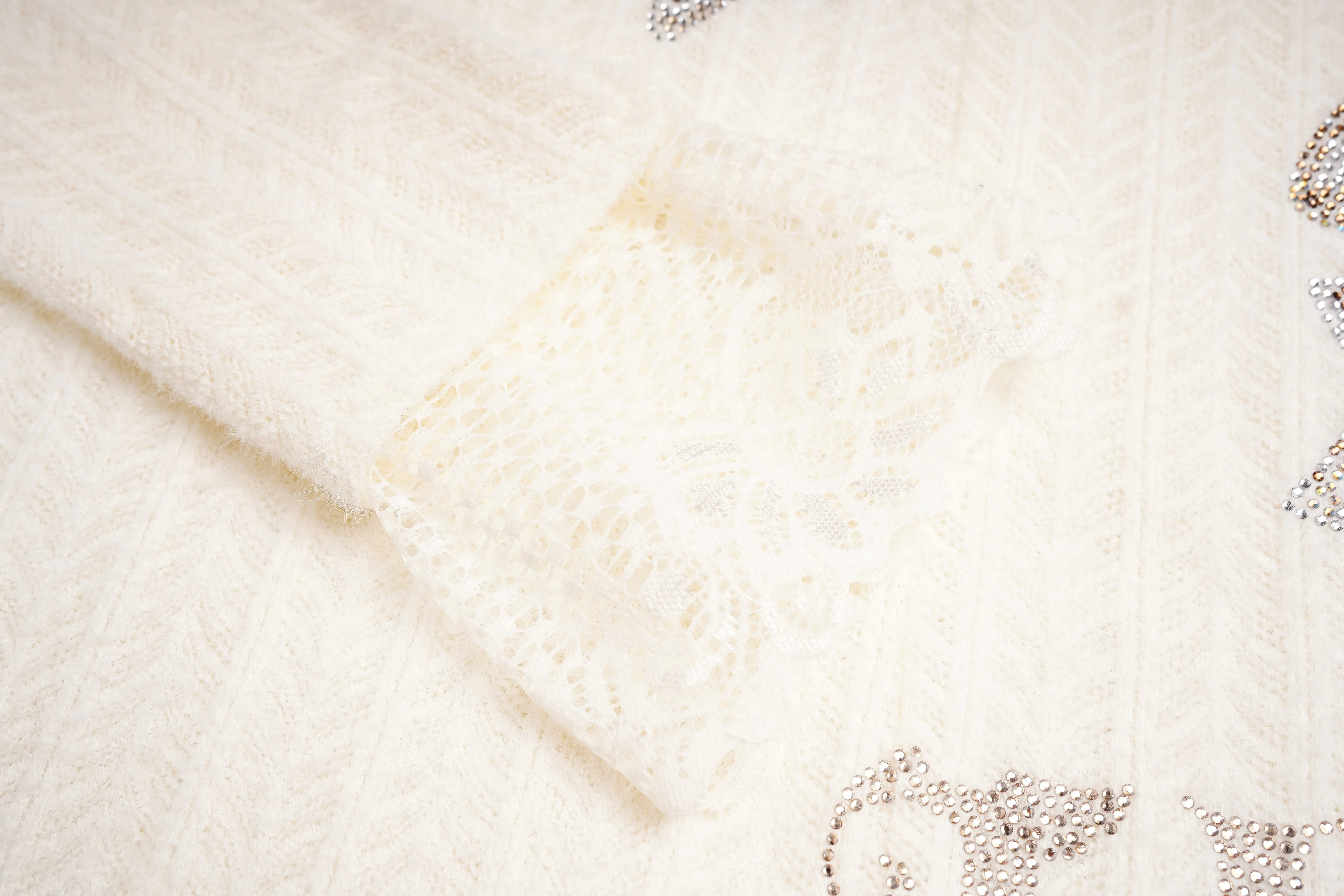 Close-up of a textured white fabric with a subtle pattern, TCH Dual-Layer Mesh V-Neck Rhinestone Bow Beige Crop Turtleneck Top