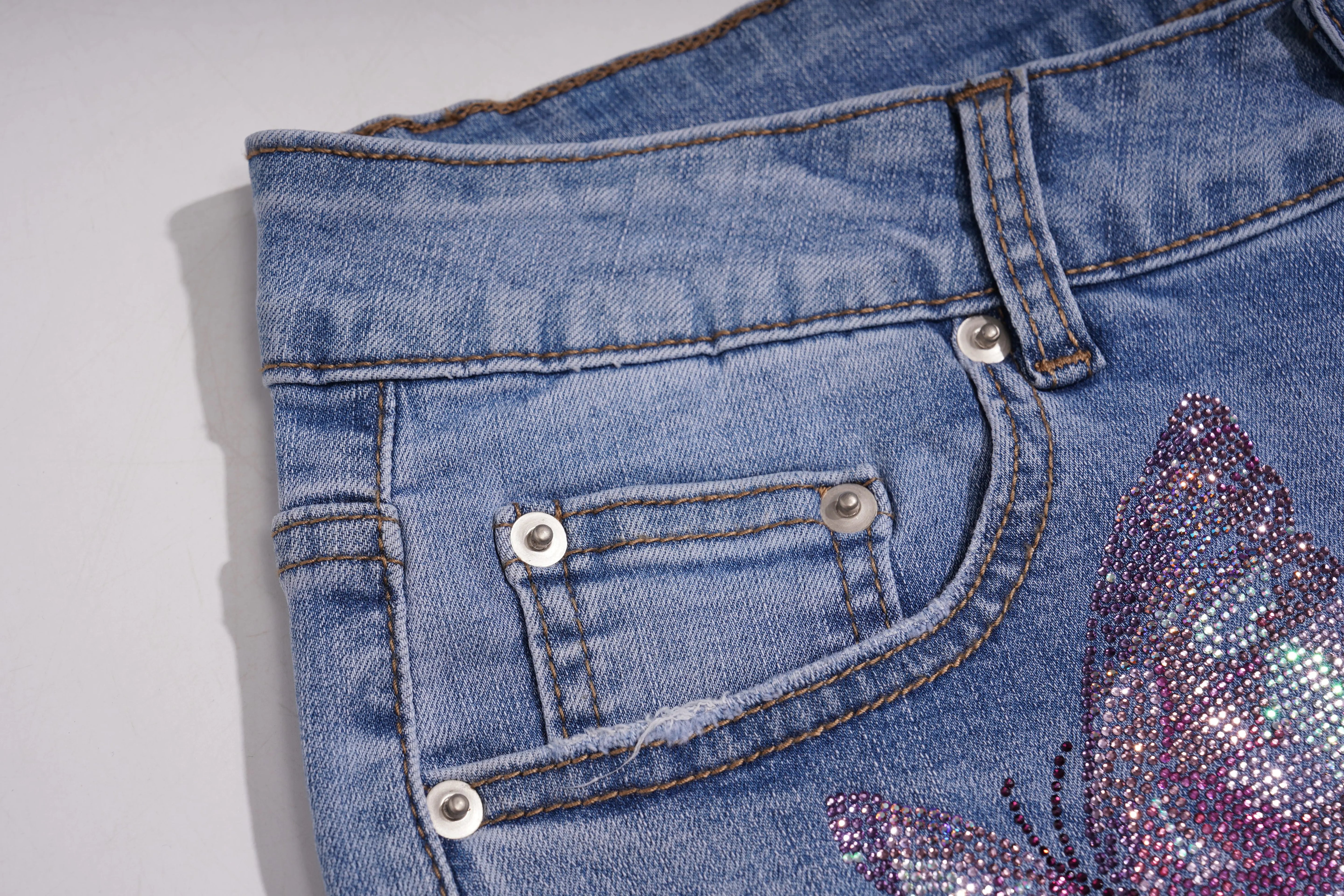 Close-up of blue denim jeans with a butterfly design on a light gray background, TCH Embroidered Rose & Rhinestone Butterfly Denim Jeans