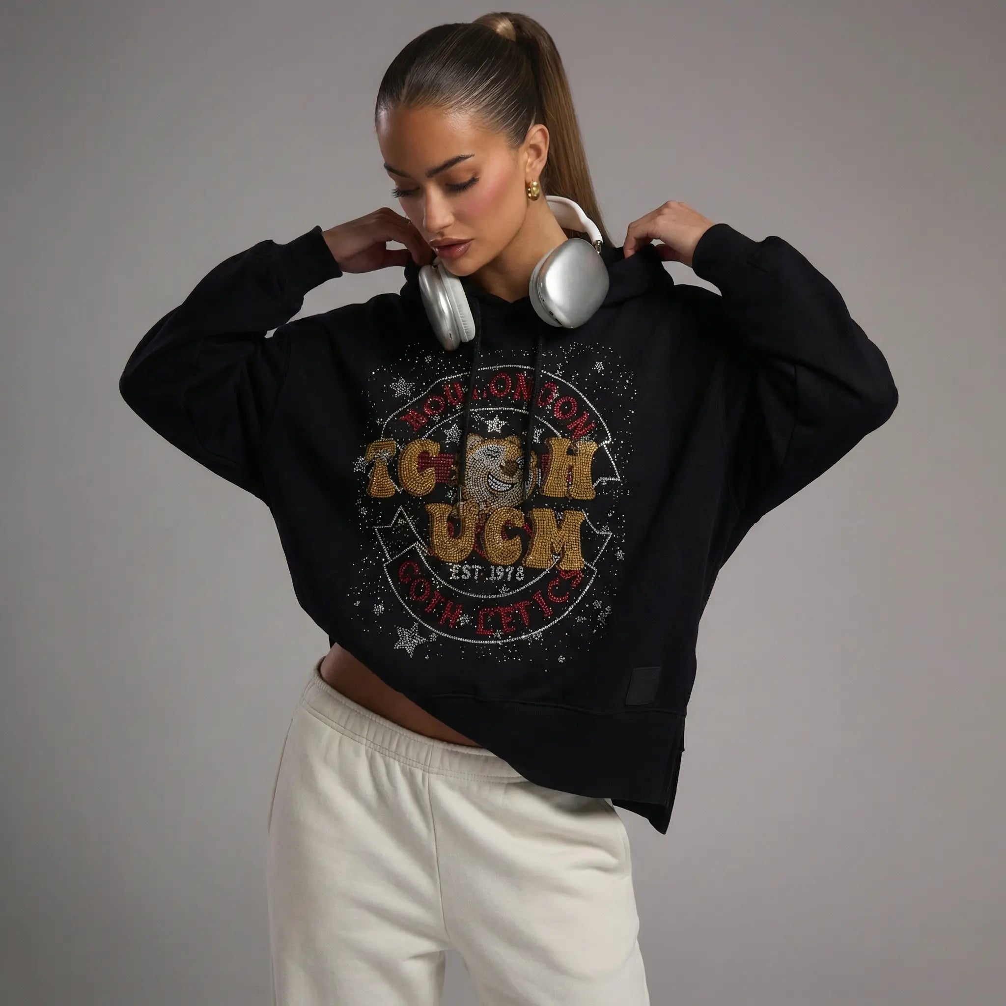 Person wearing a black hoodie with a graphic design on a gray background, TCH Embroidered TCHUCM Rhinestone Hoodie