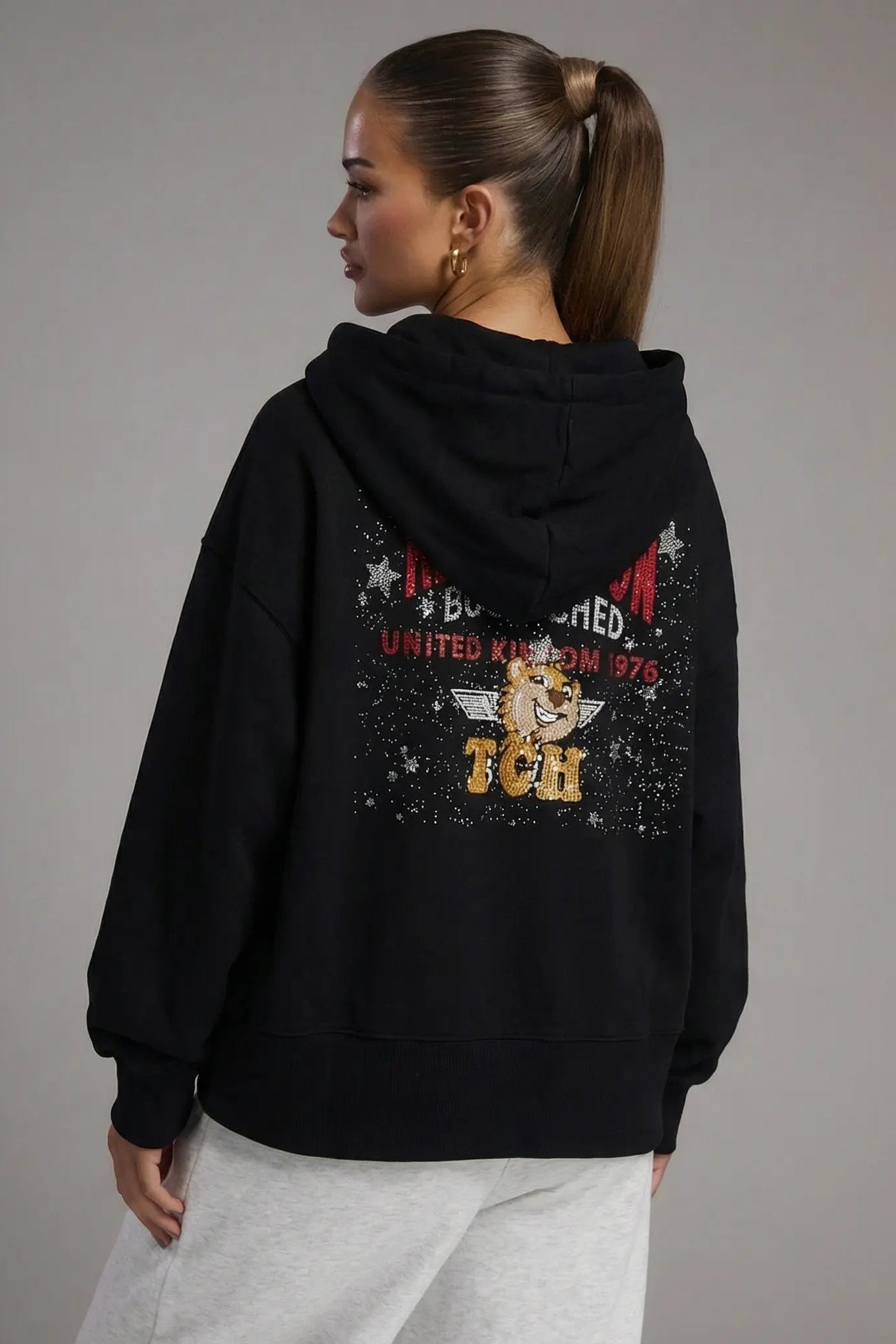 Person wearing a black hoodie with a design on the back against a gray background, TCH Embroidered TCHUCM Rhinestone Hoodie