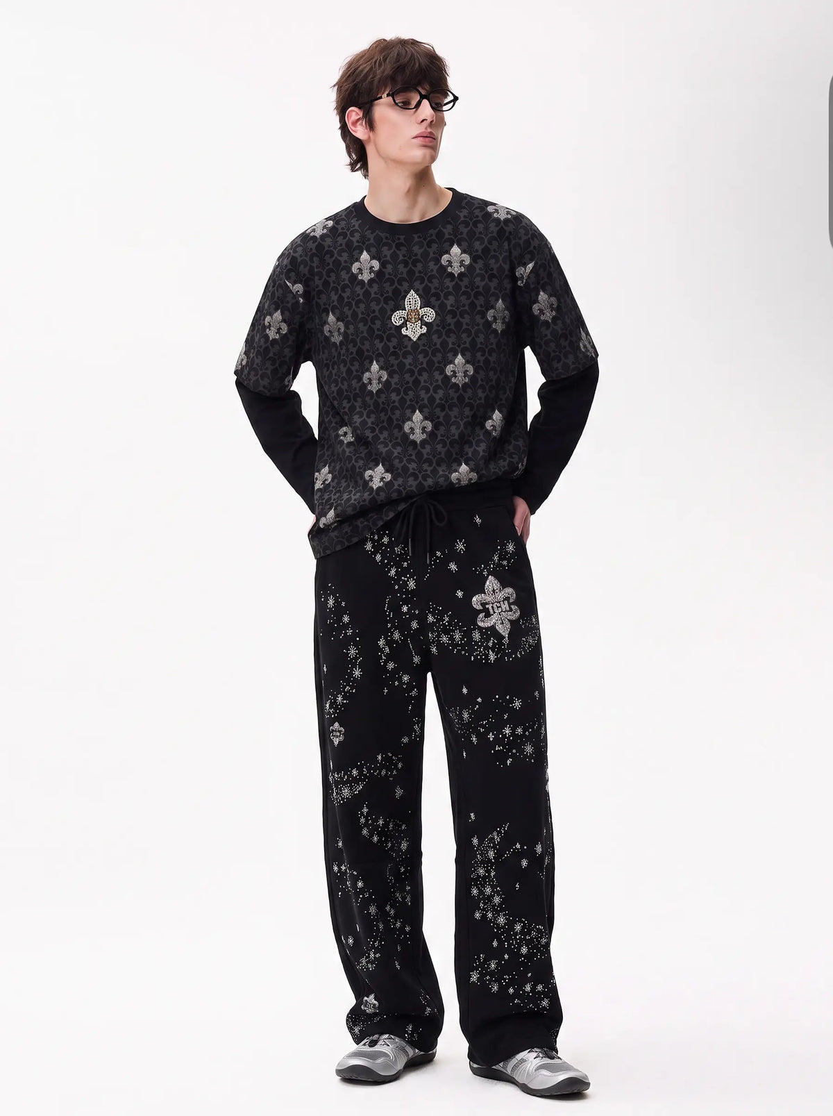 A man wearing a matching black long-sleeve knit top and wide-leg pants set with a silver-toned fleur-de-lis pattern, standing against a plain white studio background. TCH Fleur-de-Lis Pattern Layered Long Sleeve T-Shirt