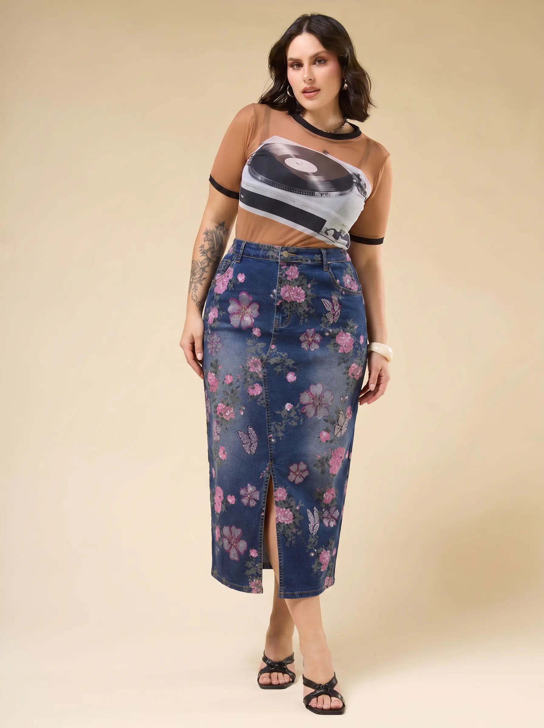 A woman modeling a sheer beige short-sleeve crop top with a black graphic print and a high-waisted blue denim midi skirt with a pink floral print, set against a solid beige studio background. TCH Floral Butterfly Print Denim Midi Skirt