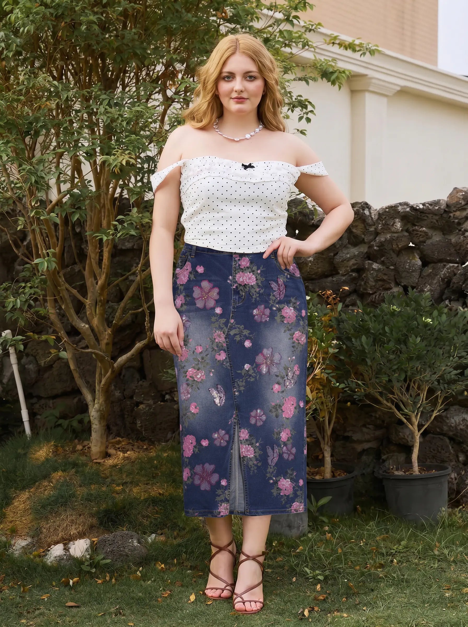 A woman stands outdoors in a garden setting wearing a white off-the-shoulder top with small black polka dots and a navy midi skirt with a pink floral print. TCH Floral Butterfly Print Denim Midi Skirt