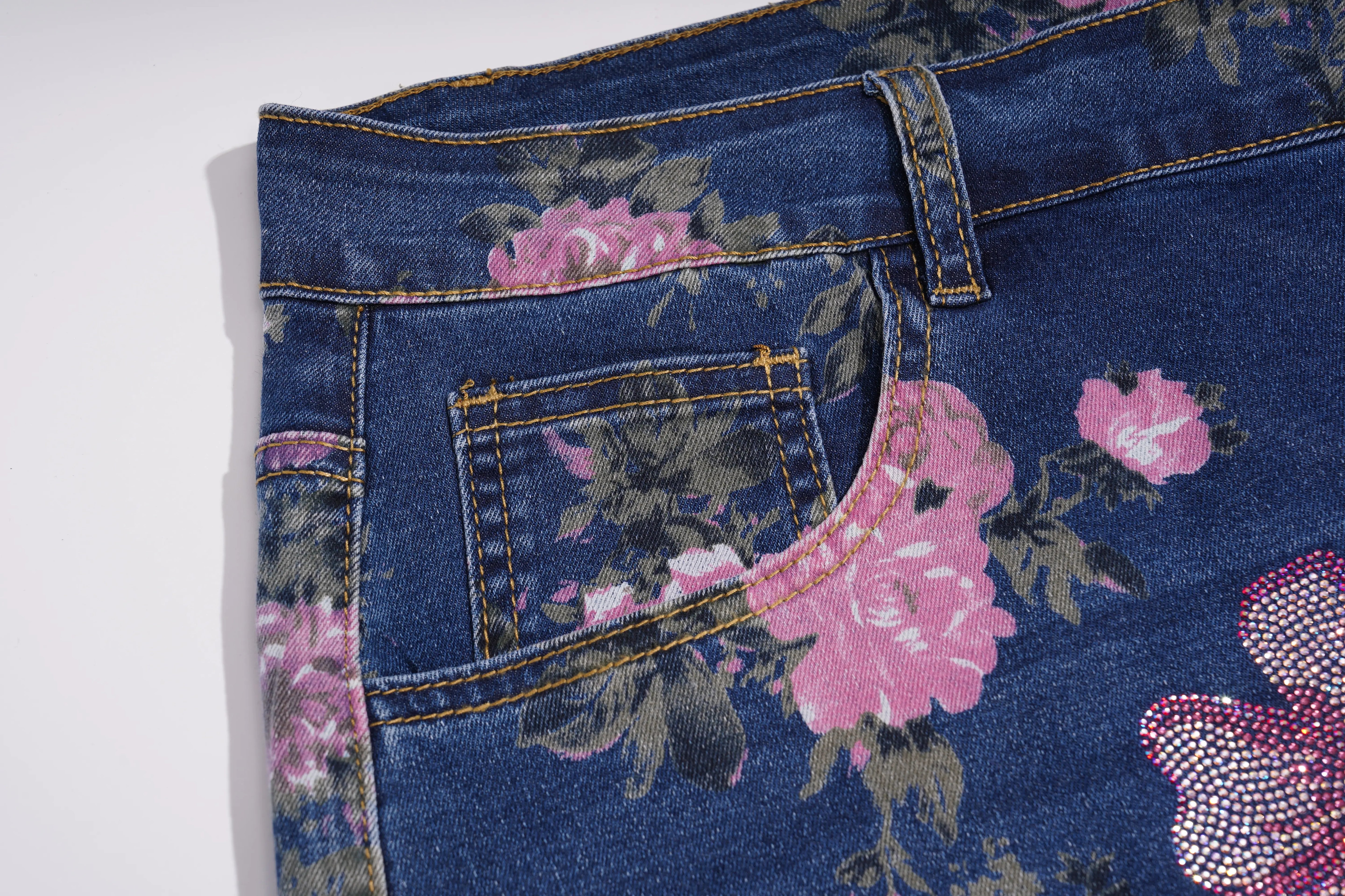 Close-up of dark blue denim jeans with a pink and green floral print, showing the waistband, belt loops, and pocket details. TCH Floral Butterfly Print Denim Midi Skirt