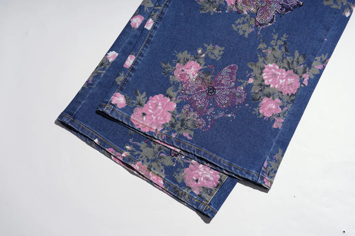 A folded pair of blue denim jeans featuring a pink and purple butterfly and floral print, displayed on a clean white background. TCH Floral Butterfly Rhinestone Wide-Leg Denim Jeans