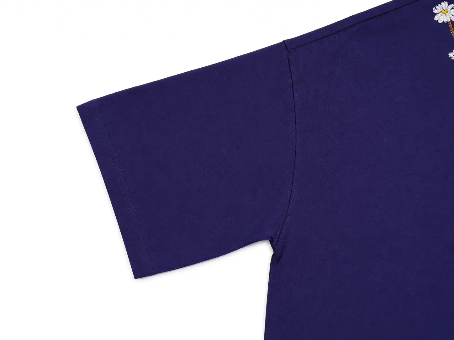 Close-up of a dark purple short-sleeve t-shirt showing the sleeve, shoulder seam, and a small white daisy graphic on the upper right chest area, set against a plain white background. TCH Floral Embroidery Graphic Navy Blue T-Shirt
