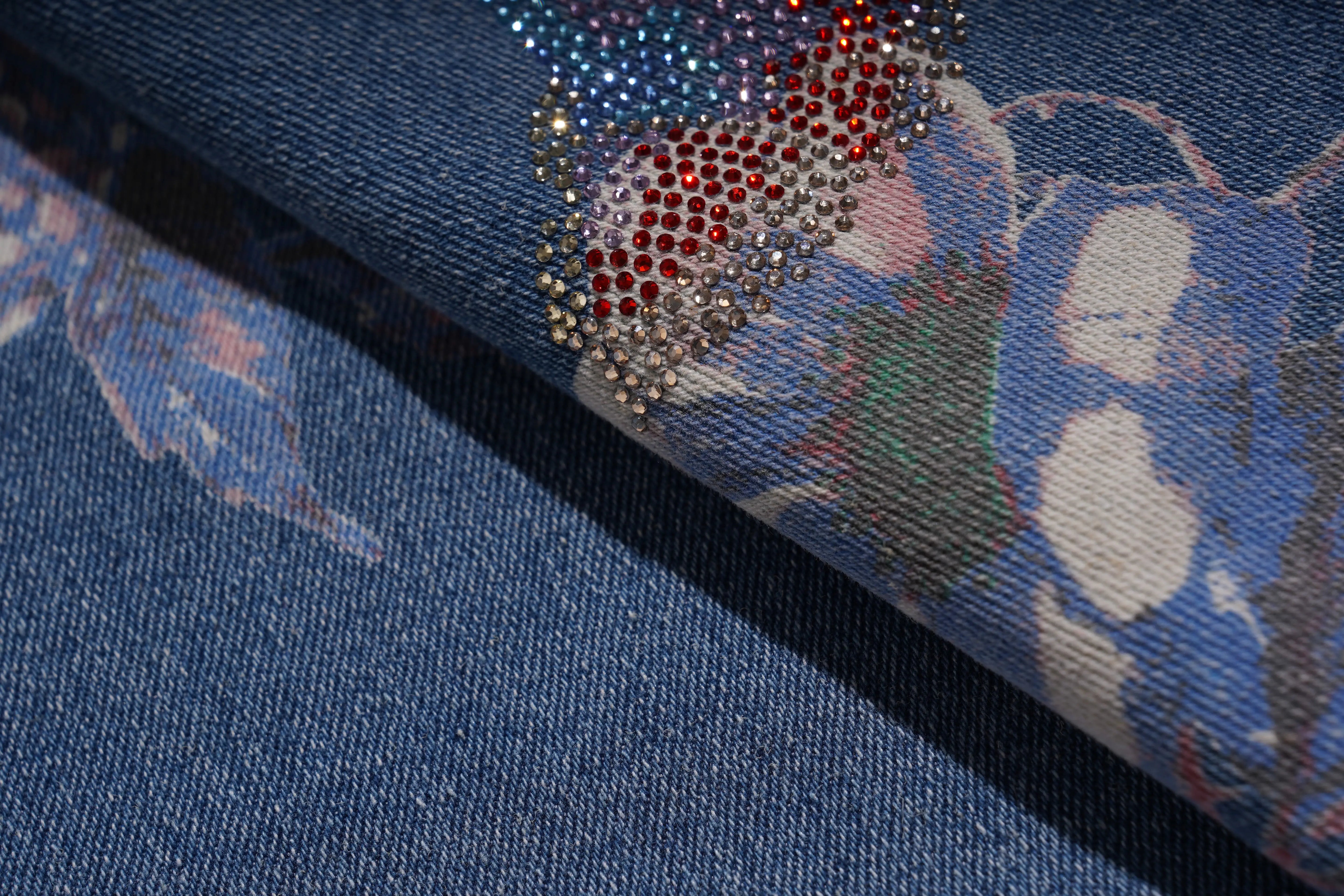Close-up of a blue fabric with floral patterns and rhinestone embellishments. TCH Floral Print Rhinestone Butterfly Denim Jeans