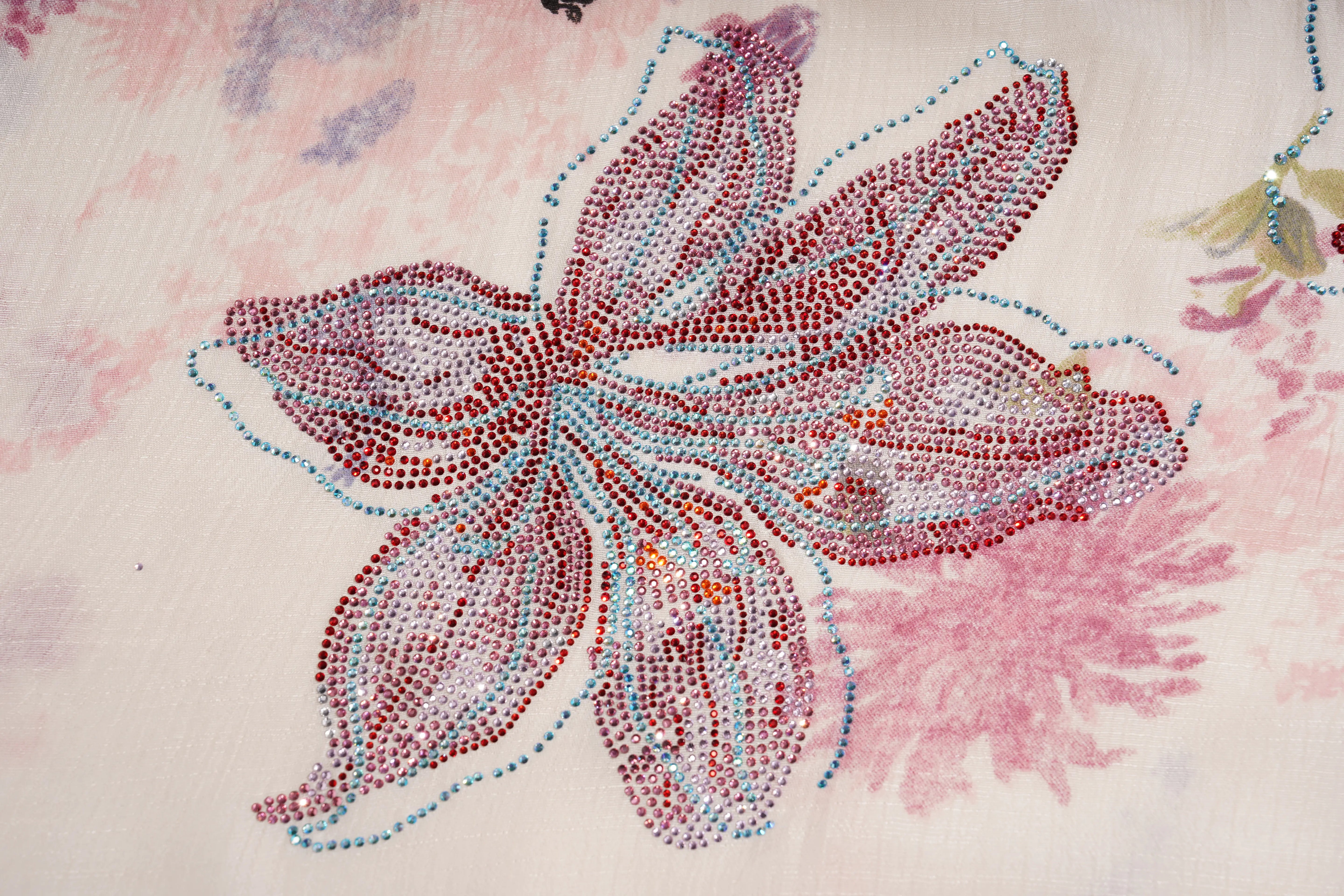 A close-up of a fabric surface featuring a large embroidered or beadwork floral motif in pink, red, and light blue on a pale pink background. TCH Floral Rhinestone Butterfly Print Short Sleeve Blouse