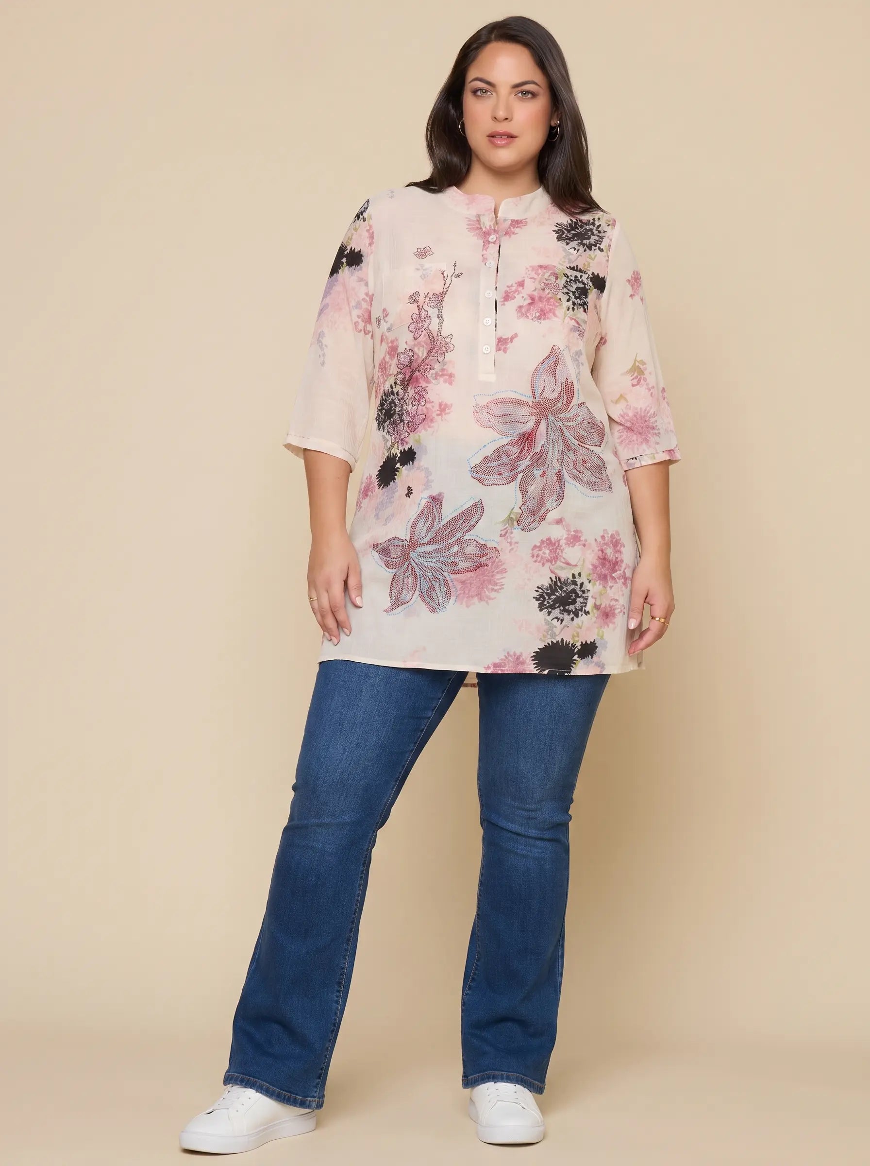 A woman modeling a light pink floral tunic top with blue jeans and white sneakers, standing against a solid beige studio background. TCH Floral Rhinestone Butterfly Print Short Sleeve Blouse