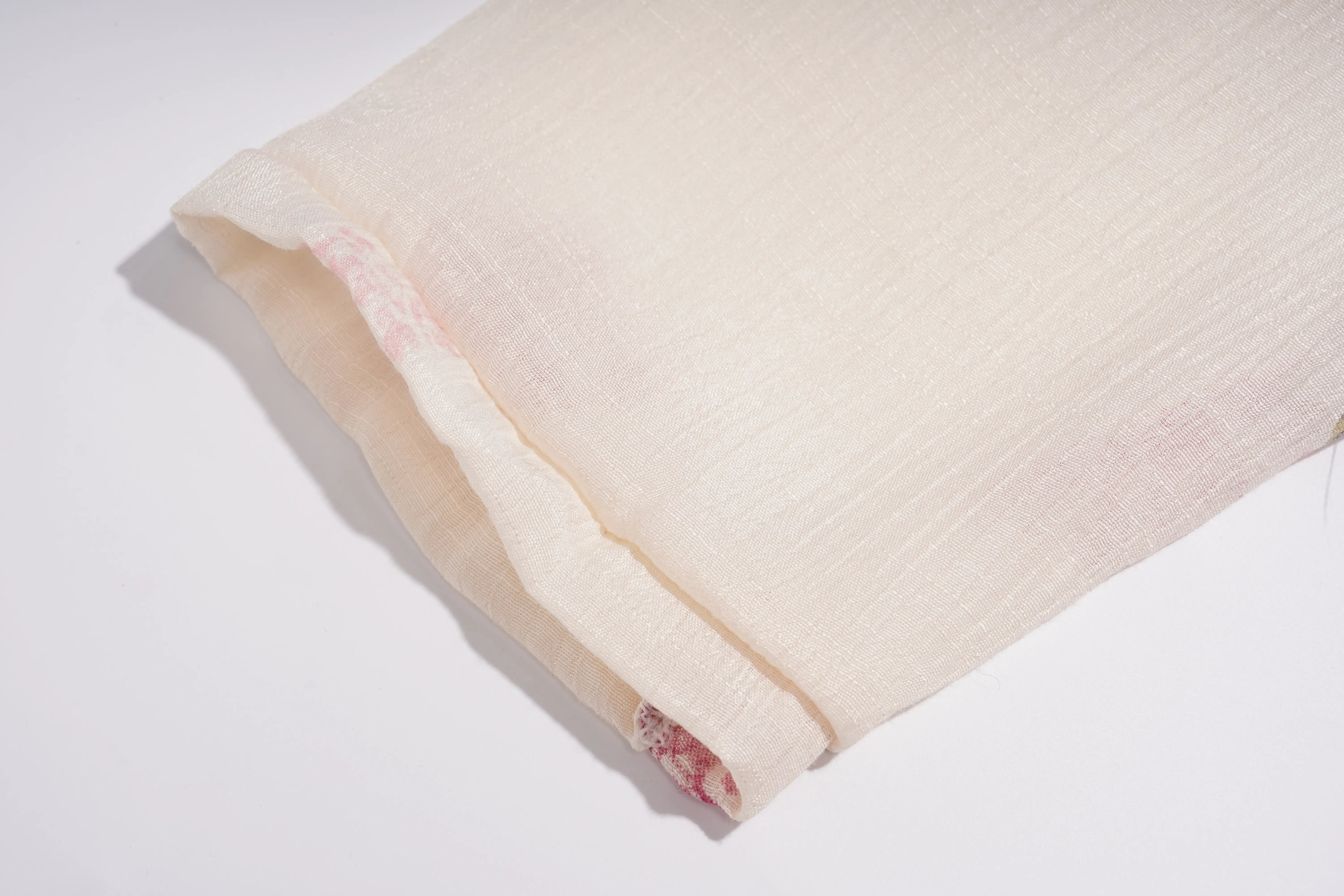 A close-up of a folded cream-colored fabric with a subtle pink pattern visible along the inner edge, set against a plain white background. TCH Floral Rhinestone Butterfly Print Short Sleeve Blouse