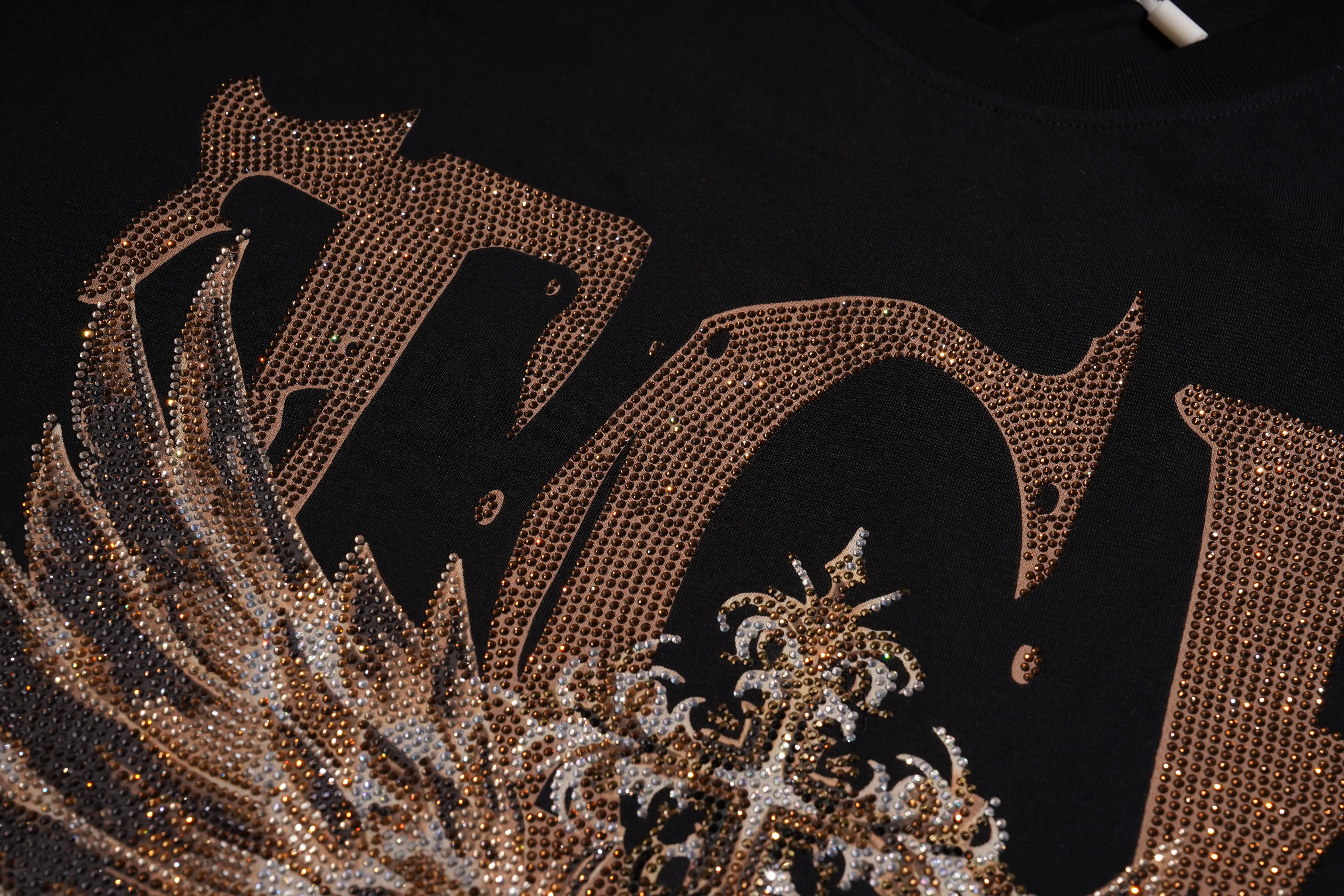 Close-up of a black garment featuring a large ornate graphic embellished with gold and silver rhinestones. TCH Golden Wing Techno Oversized Graphic T-Shirt