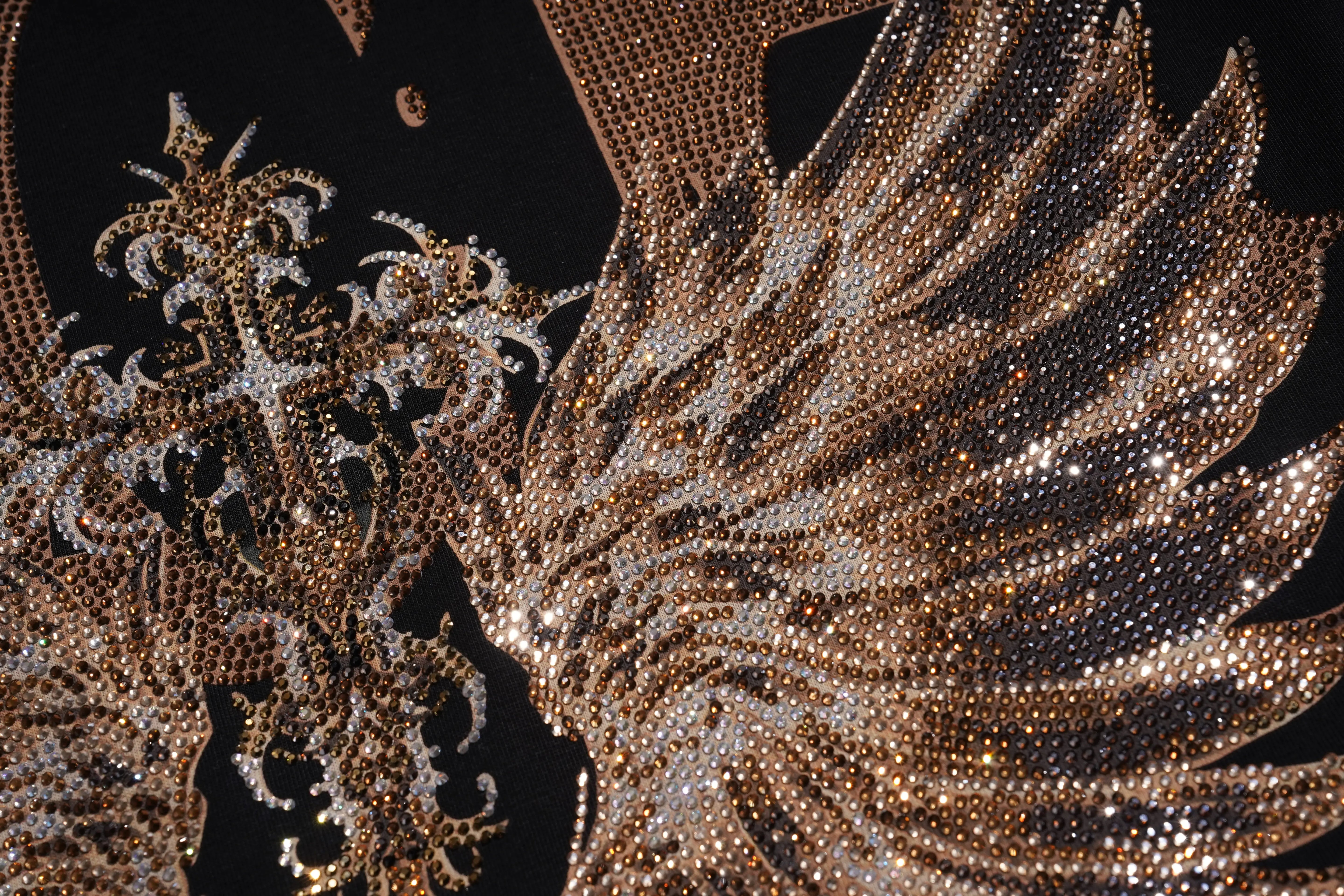 Close-up of an ornate embellished wing-like decorative element covered in metallic rose-gold and silver rhinestones on a black background. TCH Golden Wing Techno Oversized Graphic T-Shirt