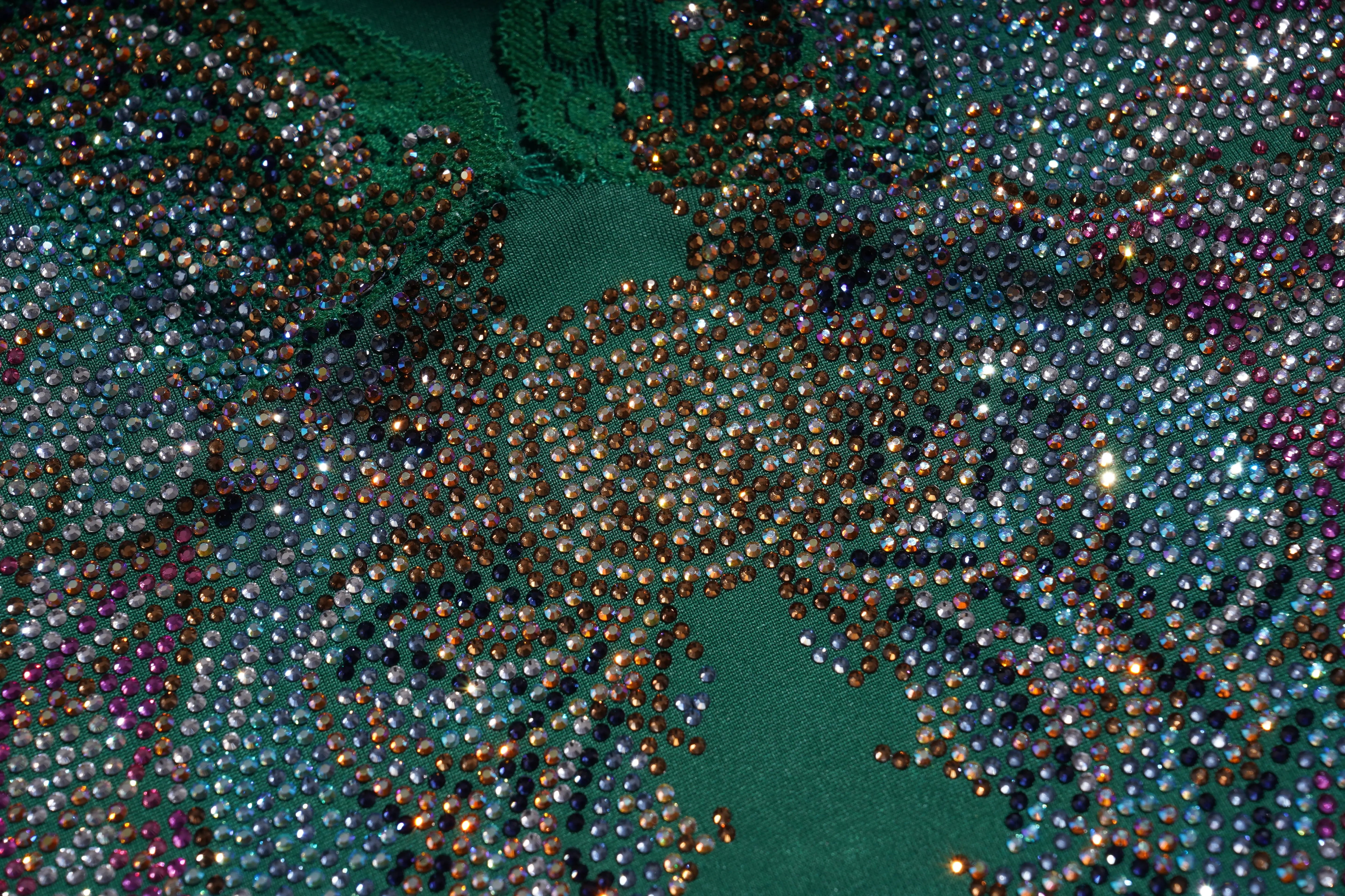 Close-up of a textured fabric with a green base and multicolored beads. TCH Green Lace Trim V-Neck Rhinestone Wing Long Sleeve Top